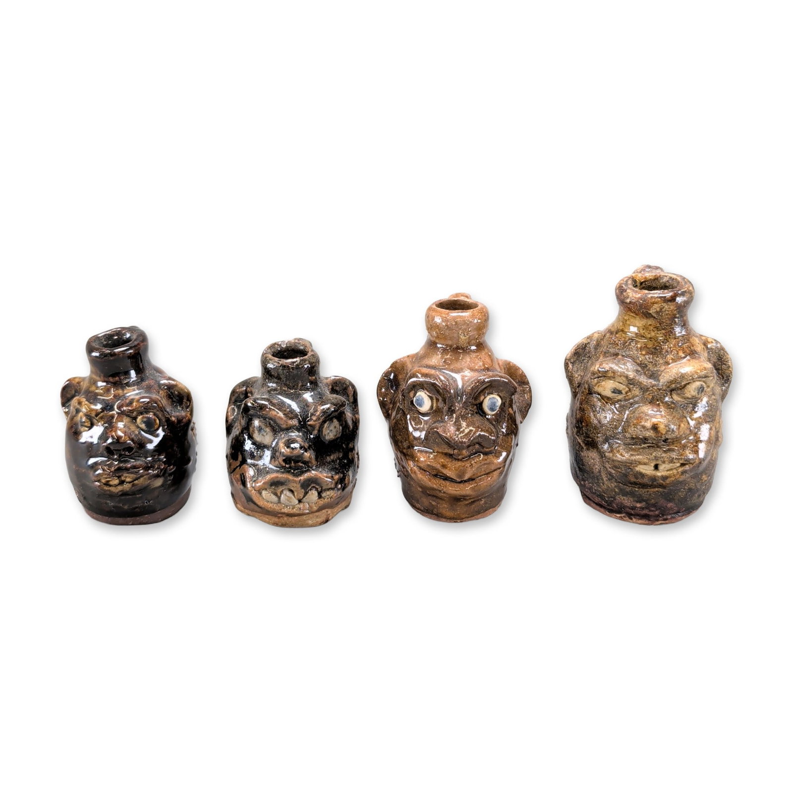 4pc Marie Rogers Pottery Georgia Folk Face Jugs: A group of miniature stoneware face jugs featuring hand-modeled facial expressions with prominent noses, ears, and mouths. The collection displays a variety of traditional glazes including a mottled