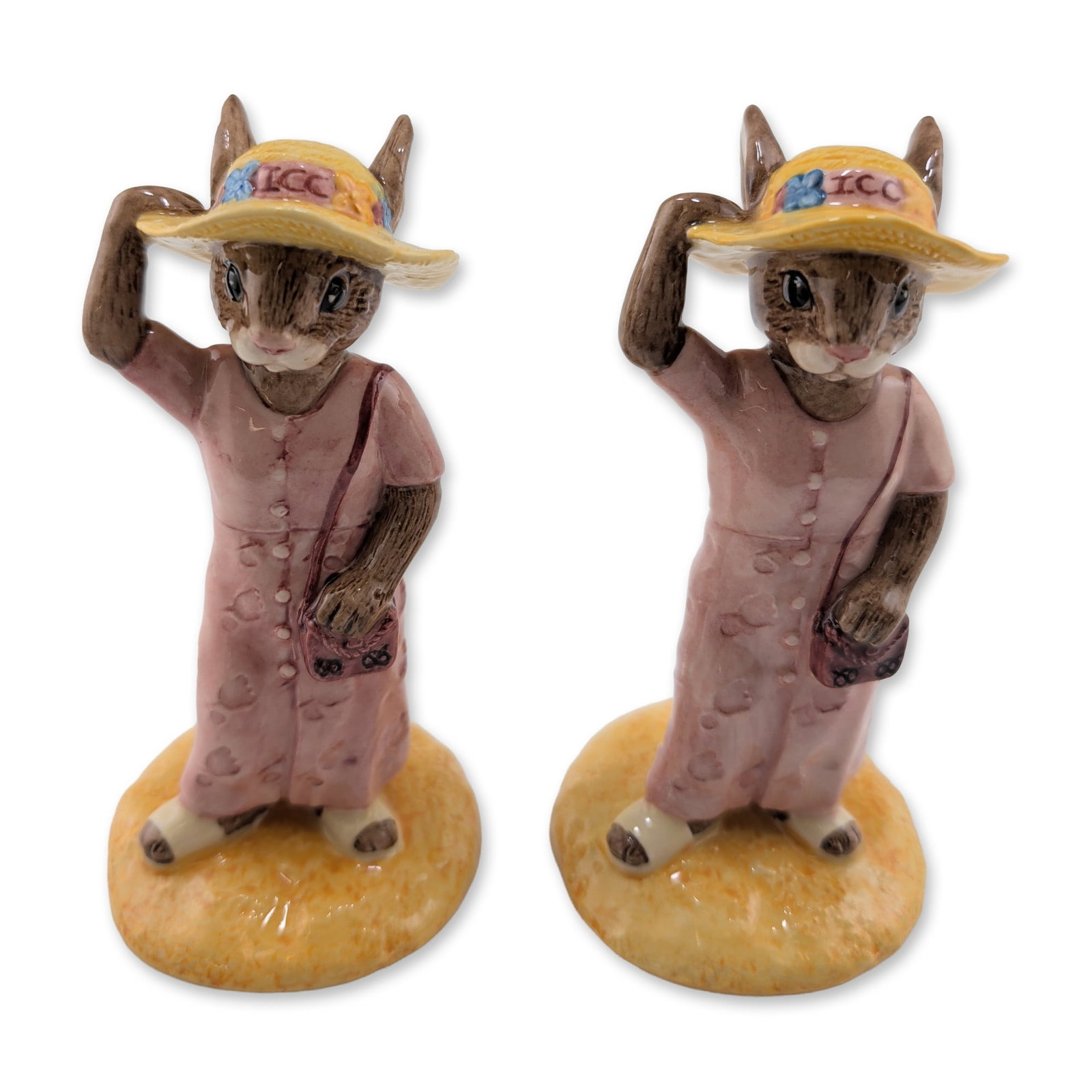 2pc Royal Doulton Porcelain Sightseer Bunnykins Figurines: Royal Doulton. Pair of Bunnykins figurines in glazed porcelain titled Sightseer, model DB 215. Each figure depicts a female rabbit character dressed for travel in a pink patterned coat and a yellow st