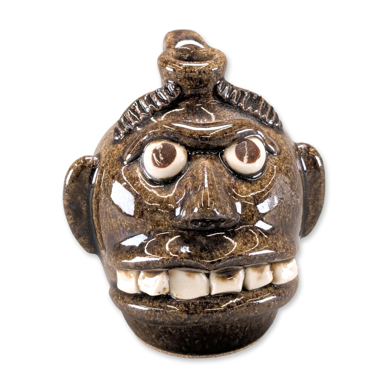 Otis Norris Pottery Folk Art Face Jug: The piece displays stylized features including bulging white clay eyes with dark pupils, an open mouth with individually modeled white teeth, and large ears. A textured handle-like protrusion sits at 