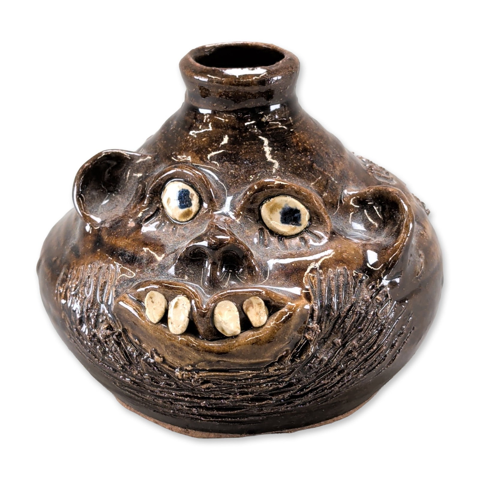 Marie Rogers Pottery Georgia Folk Art Face Jug: The vessel features a globular body with a single tapered spout and a rear strap handle. The surface is finished in a dark brown, high-gloss glaze. The grotesque applied face includes bulging eyes wit