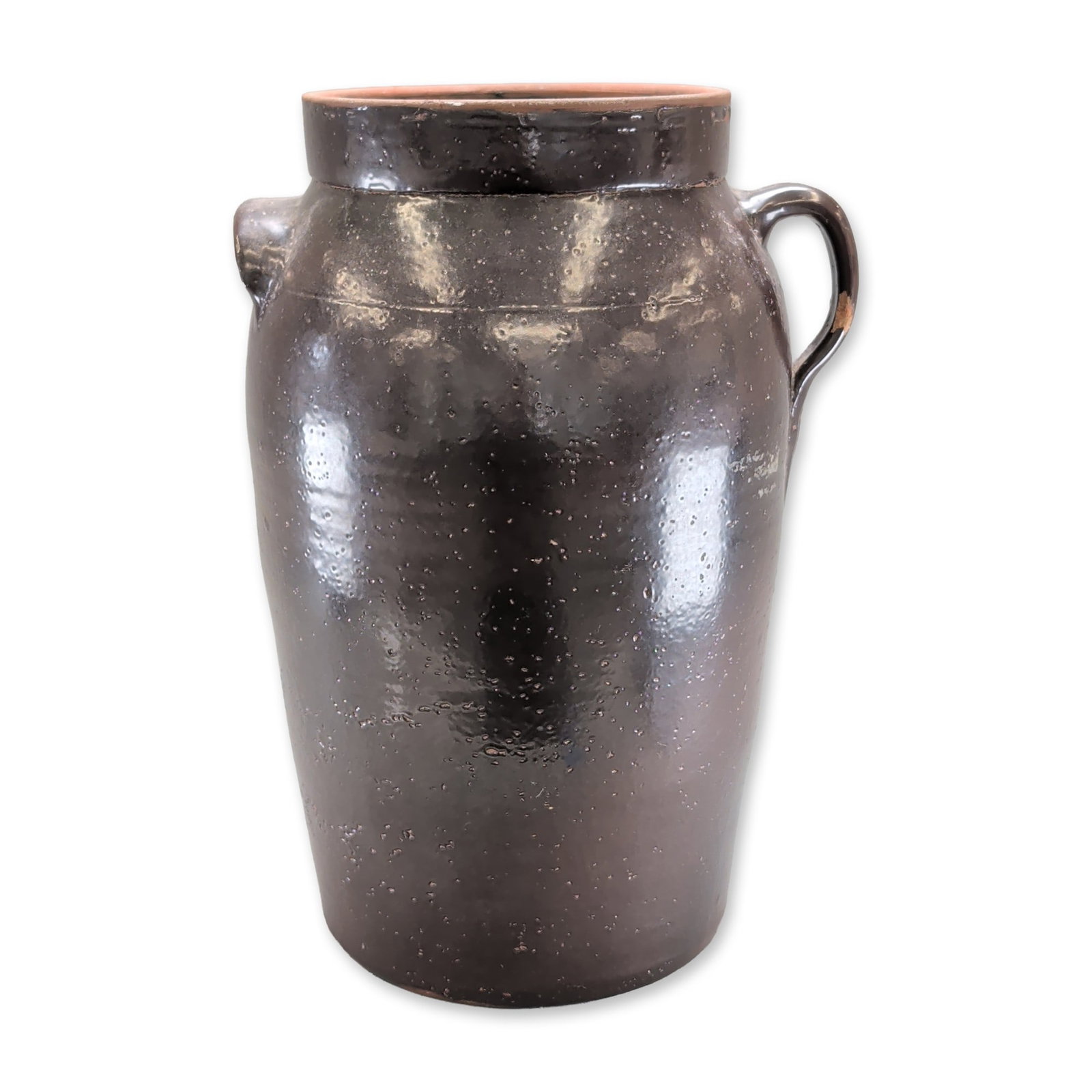 Stoneware Butter Churn Crock: The vessel features a glossy dark brown Albany-type slip glaze with an orange peel texture. An unusual handle arrangement includes one vertical loop handle and one horizontal lug handle. The shoulder 
