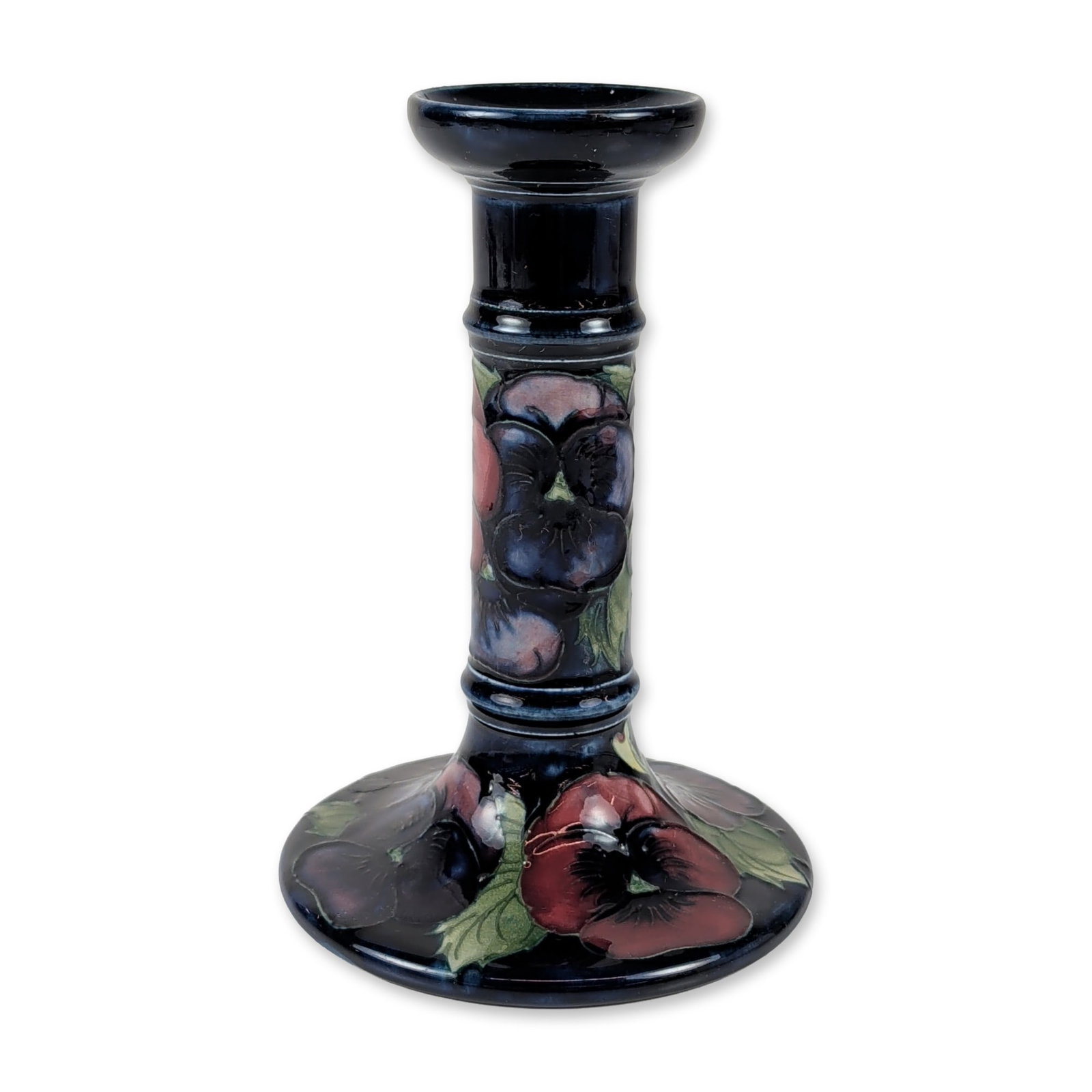 Moorcroft Pansy Pattern Art Pottery Candlestick: Moorcroft pottery candlestick in the Pansy pattern, featuring tube-lined and hand-painted decoration on a dark cobalt blue ground. The earthenware form includes a flared rim and central column with tw