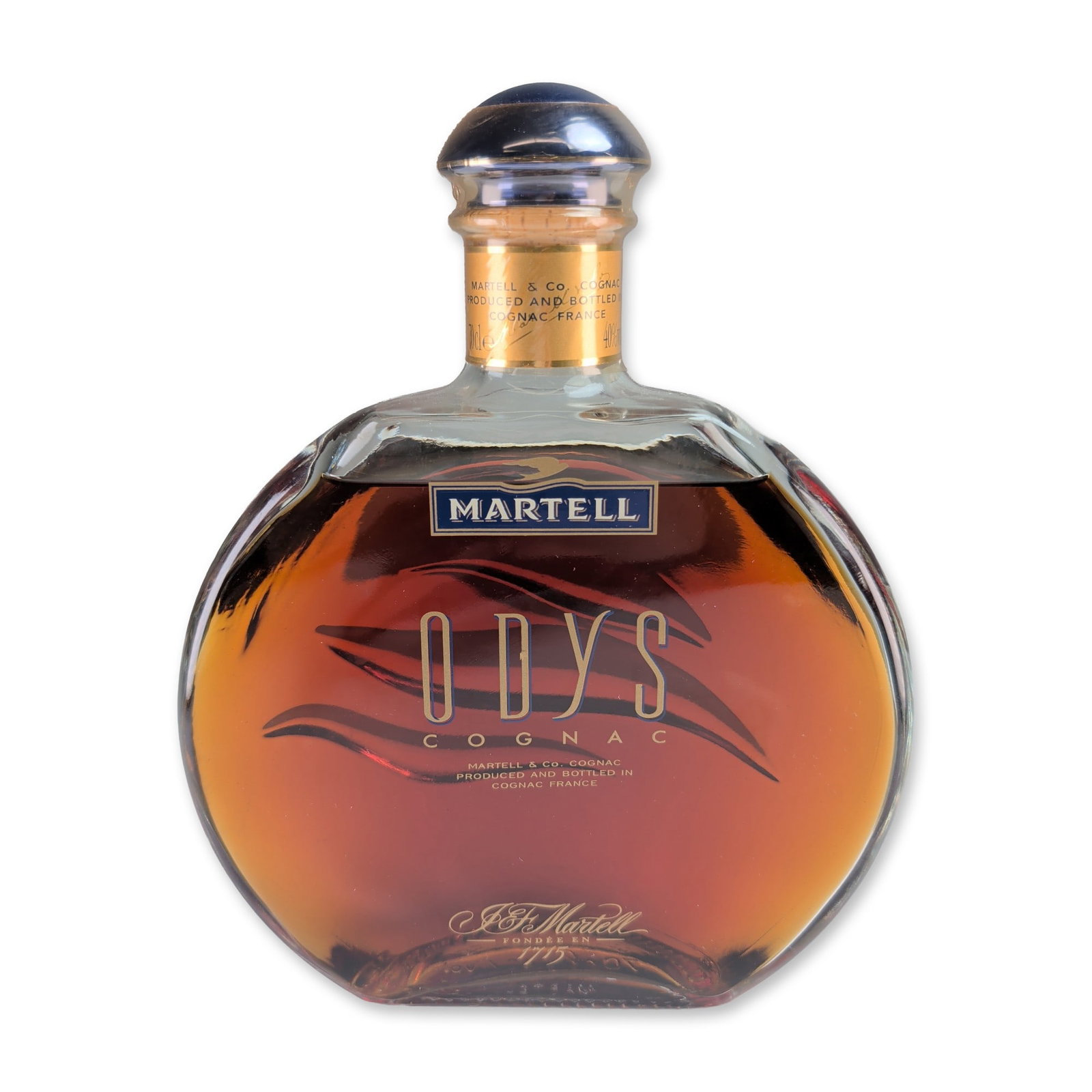 Martell France Odys Cognac Bottle Decanter: Martell, France, Odys Cognac presented in a circular flat-sided glass decanter with wave-like decorative ridges on the reverse. The bottle is sealed with a dark blue cap over a cork stopper and a gold