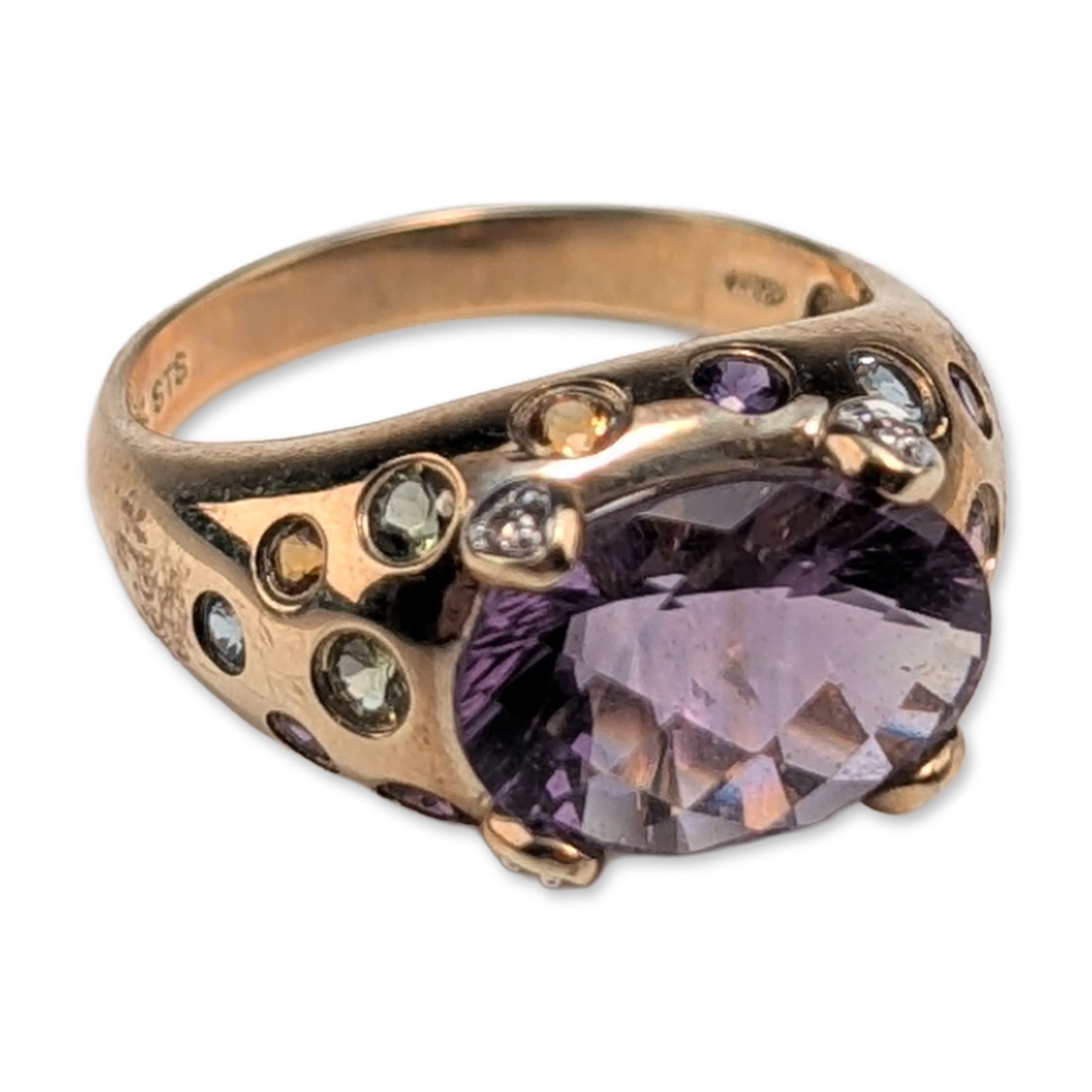 STS 10K Yellow Gold Amethyst Cocktail Ring: STS cocktail ring in 10K yellow gold, featuring a center oval checkerboard-cut purple amethyst secured by four prongs. A round-cut diamond accents each prong. The wide, domed band features circular