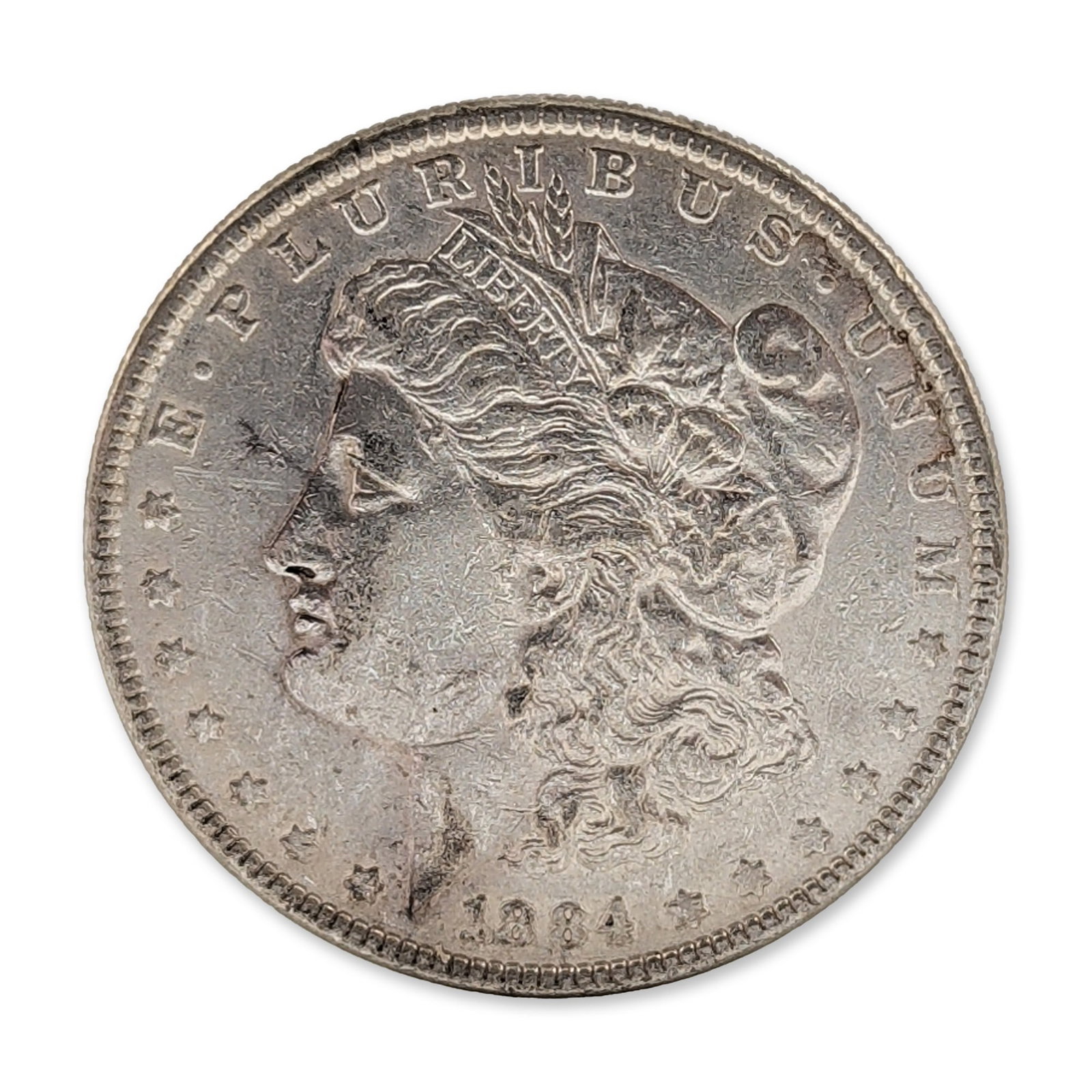 1884 US Morgan Silver Dollar Coin: US 1884 Morgan Silver Dollar struck at the Philadelphia mint. 90% silver composition. Obverse features a left-facing profile of Liberty with the legend E PLURIBUS UNUM and date 1884. Reverse depicts a