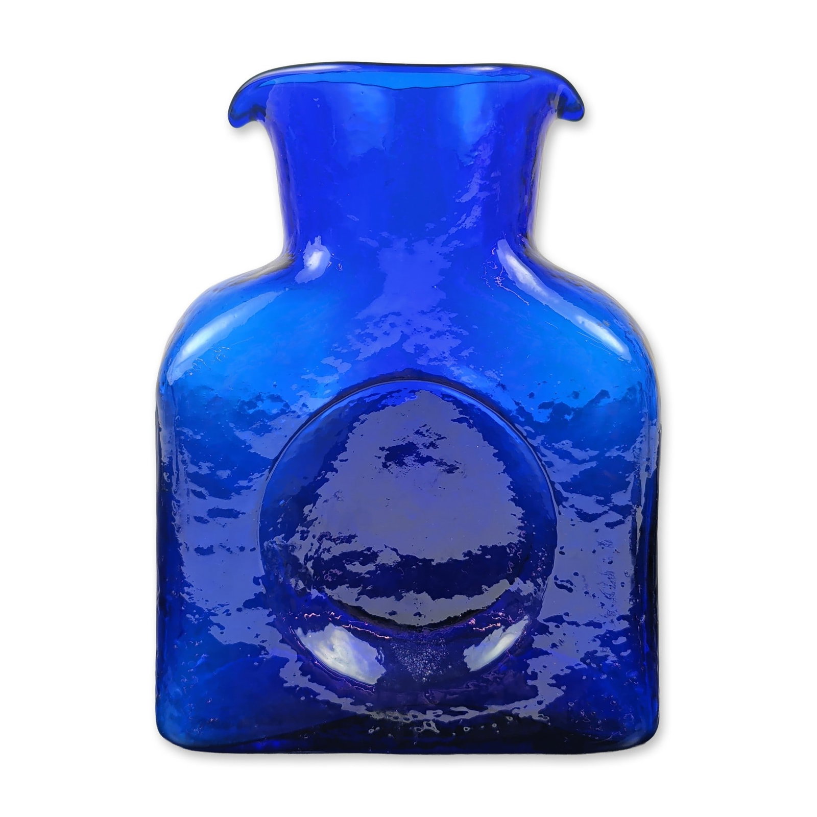 Blenko Mid-Century Hammered Cobalt Glass Water Bottle: Mid-century modern art glass decanter in translucent cobalt blue, featuring a rectangular form with a deep circular indentation to the center of the front and back faces. The mold-blown vessel exhibit