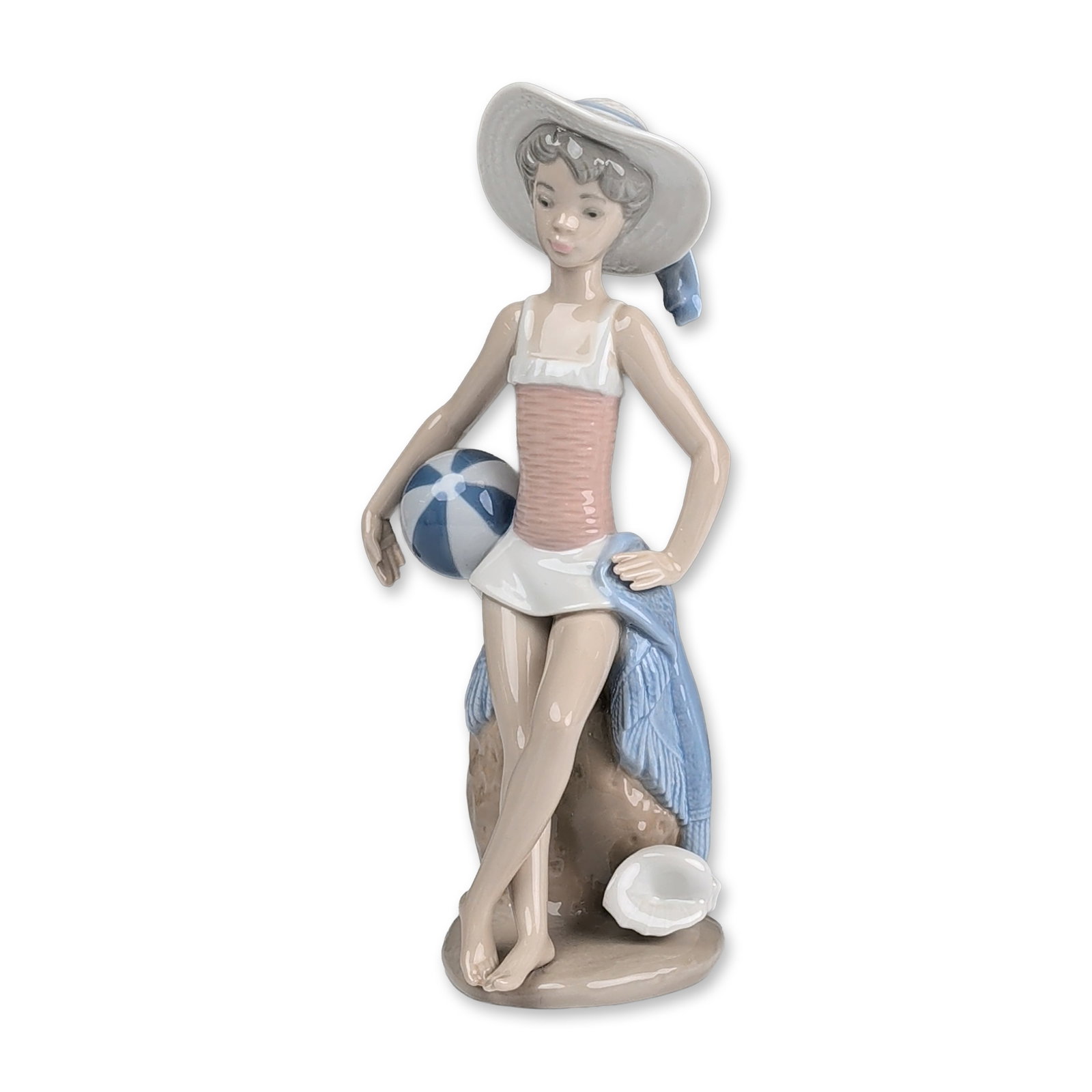 Lladro Glazed Porcelain Figurine, Summer 01005219: Lladro (Spain) glazed polychrome porcelain figurine, model 5219 titled Summer. The piece depicts a young woman in beach attire, wearing a wide-brimmed white hat with a blue ribbon, a pink ribbed swims