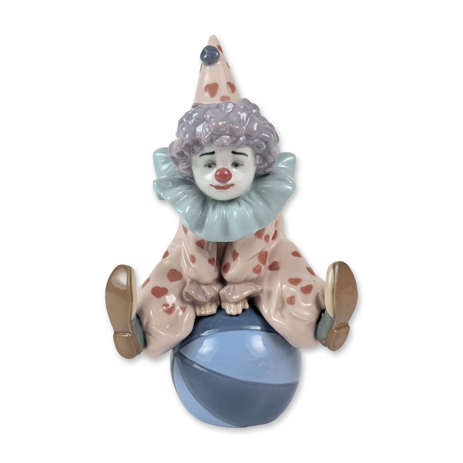 Lladro Porcelain Figurine, Having a Ball 1005813: A Lladro glazed porcelain figurine titled Having a Ball, model number 1005813. The piece depicts a seated clown with textured lavender hair and a tall, pointed hat. The figure is dressed in a pink-col