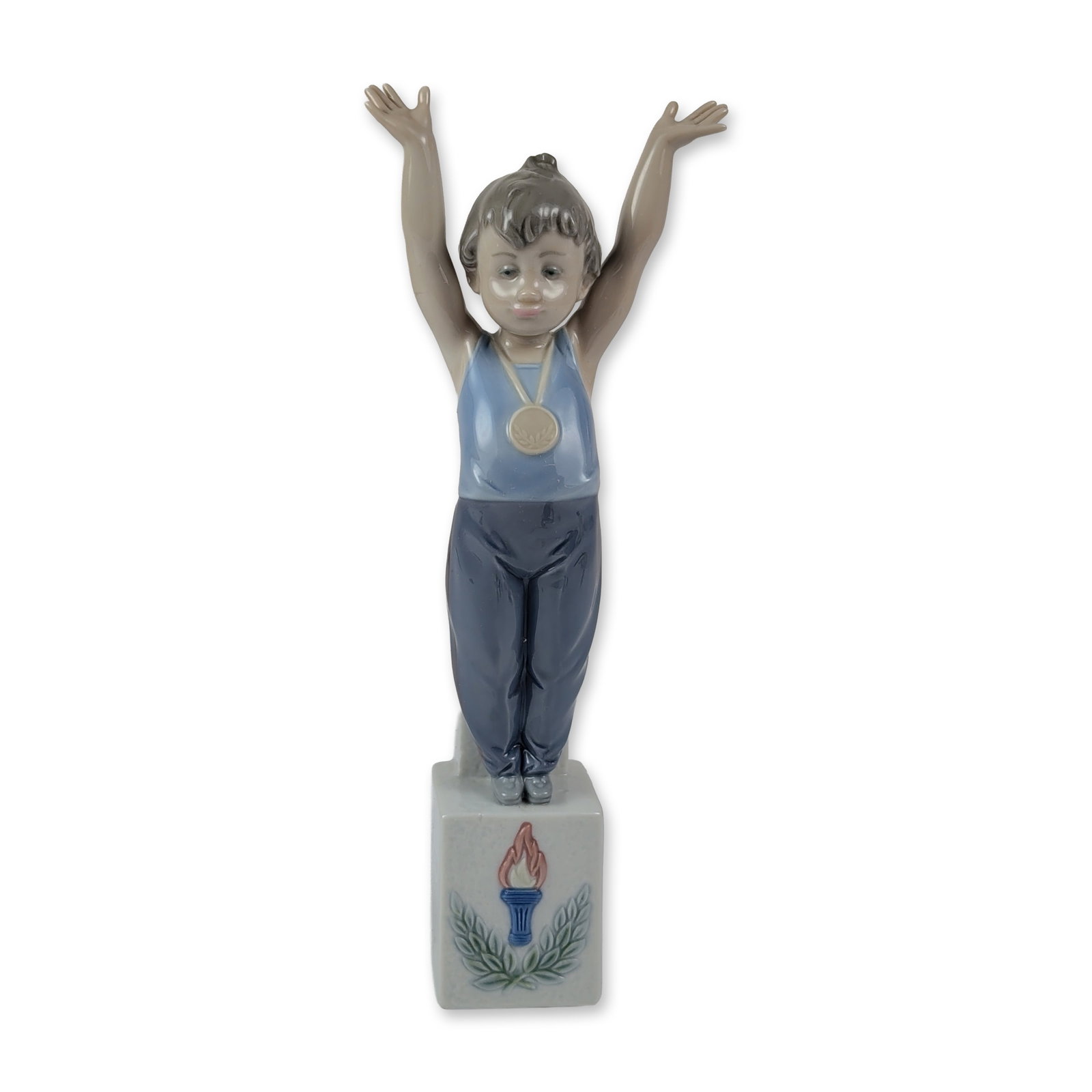 Lladro Porcelain Figurine, Olympic Champion 1005871: Designed by Antonio Ramos. This glossy finish figure depicts a young male athlete in a celebratory pose atop a square pedestal decorated with low-relief motifs of a flaming torch and laurel leaves. Th