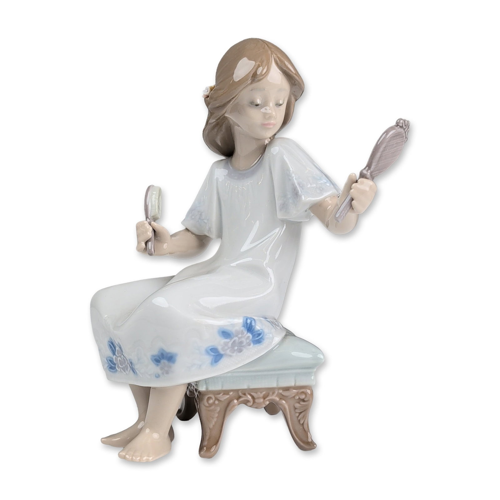 Lladro Porcelain Figurine, I Feel Pretty 01005678: Glazed porcelain figurine depicting a young girl seated on a blue-cushioned stool while grooming herself with a hand mirror and hairbrush. The figure wears a white dress decorated with blue floral mot