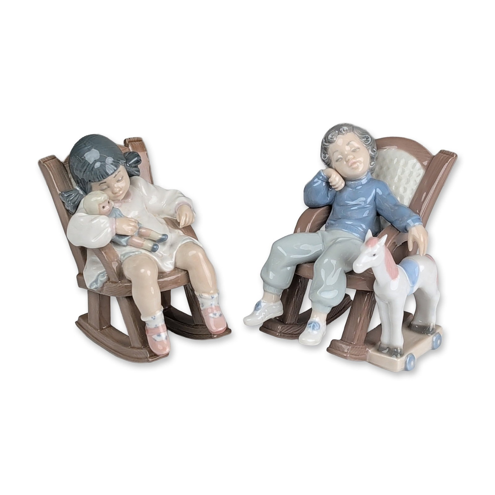 2pc Lladro Porcelain Figurines, All Tuckered Out 01005846 & Naptime 01005448: Lladro Spanish glazed porcelain figurines depicting a young girl and boy asleep in rocking chairs. The first figurine features a girl in a white nightgown holding a doll, seated in a wood-grain textur