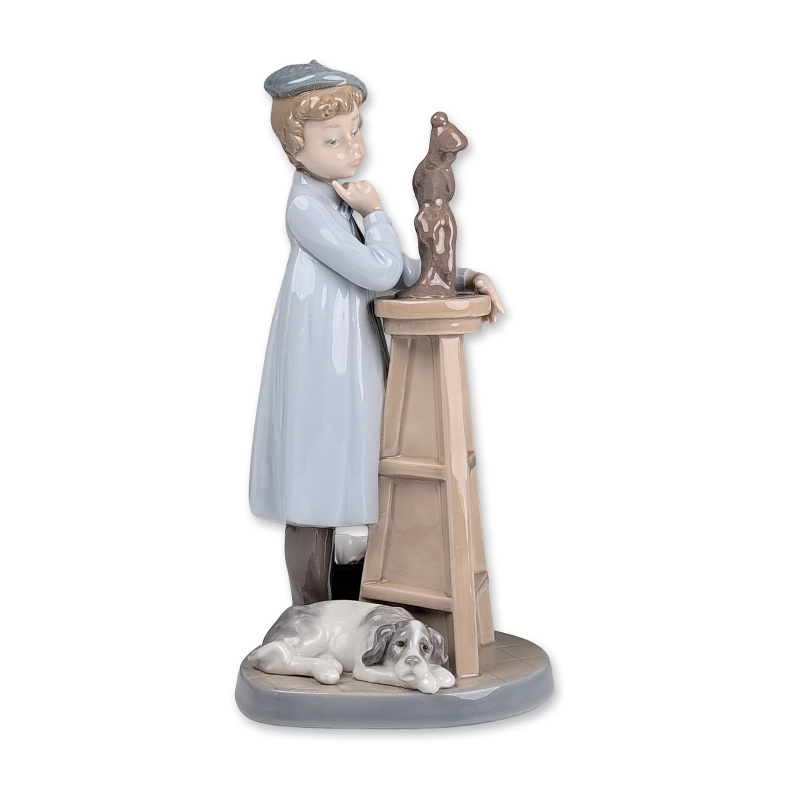 Lladro Porcelain Figurine, Little Sculptor 01005358: The Little Sculptor depicting a young boy in a blue artist smock and grey beret contemplating a sculpture on a pedestal with a spotted dog at his feet. A blue printed mark on the base features a bell 