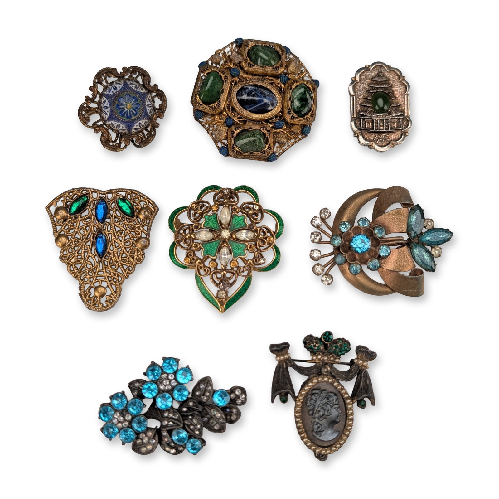 Collection of Eight Vintage Costume Jewelry Brooches: Collection of eight vintage costume jewelry brooches featuring various Victorian-revival and mid-century modern designs. The assortment includes a gold-tone filigree brooch set with four tumbled green