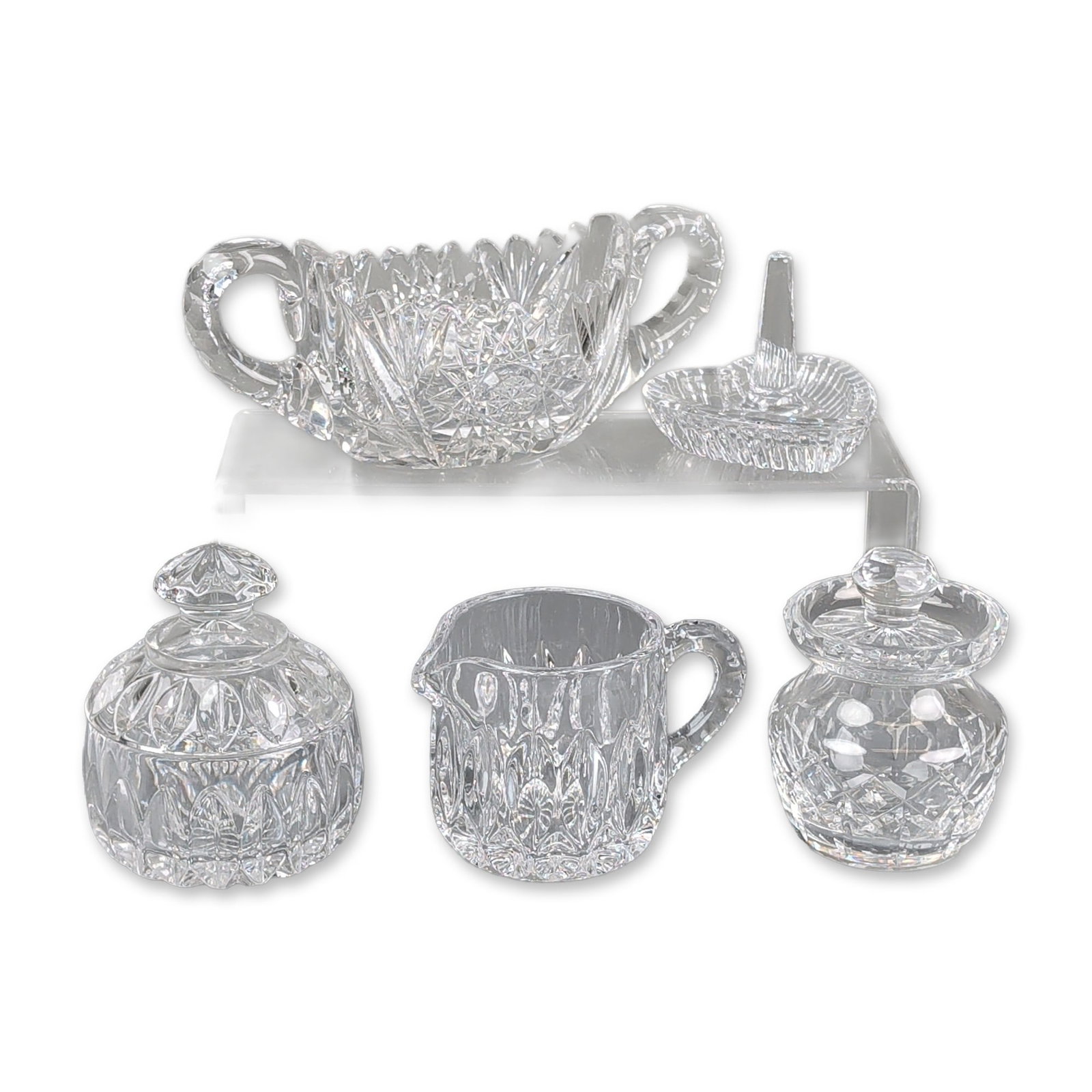 5pc Cut Glass Tableware Group: This collection features a handled basket, a creamer, two lidded condiment jars, and a heart-shaped ring holder. The creamer and one jar are decorated with vertical oval thumbprint cuts, while the oth