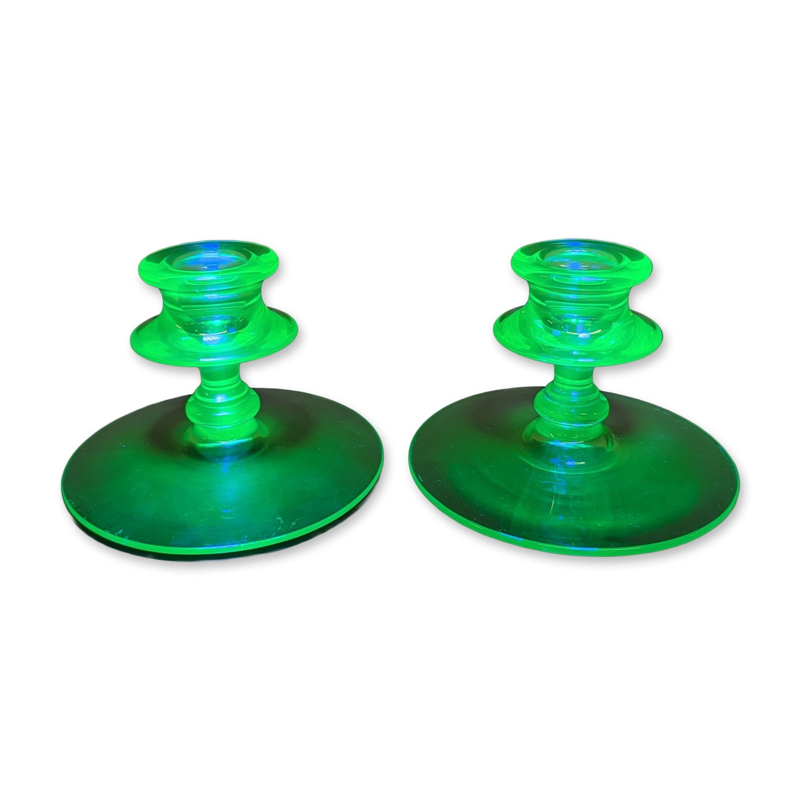 2pc Art Deco Uranium Glass Candlesticks: A pair of Art Deco style candlesticks in transparent green uranium glass, featuring a flared funnel-shaped cup over a ringed, multi-knopped stem on a wide, flat circular disk base. The glass compositi