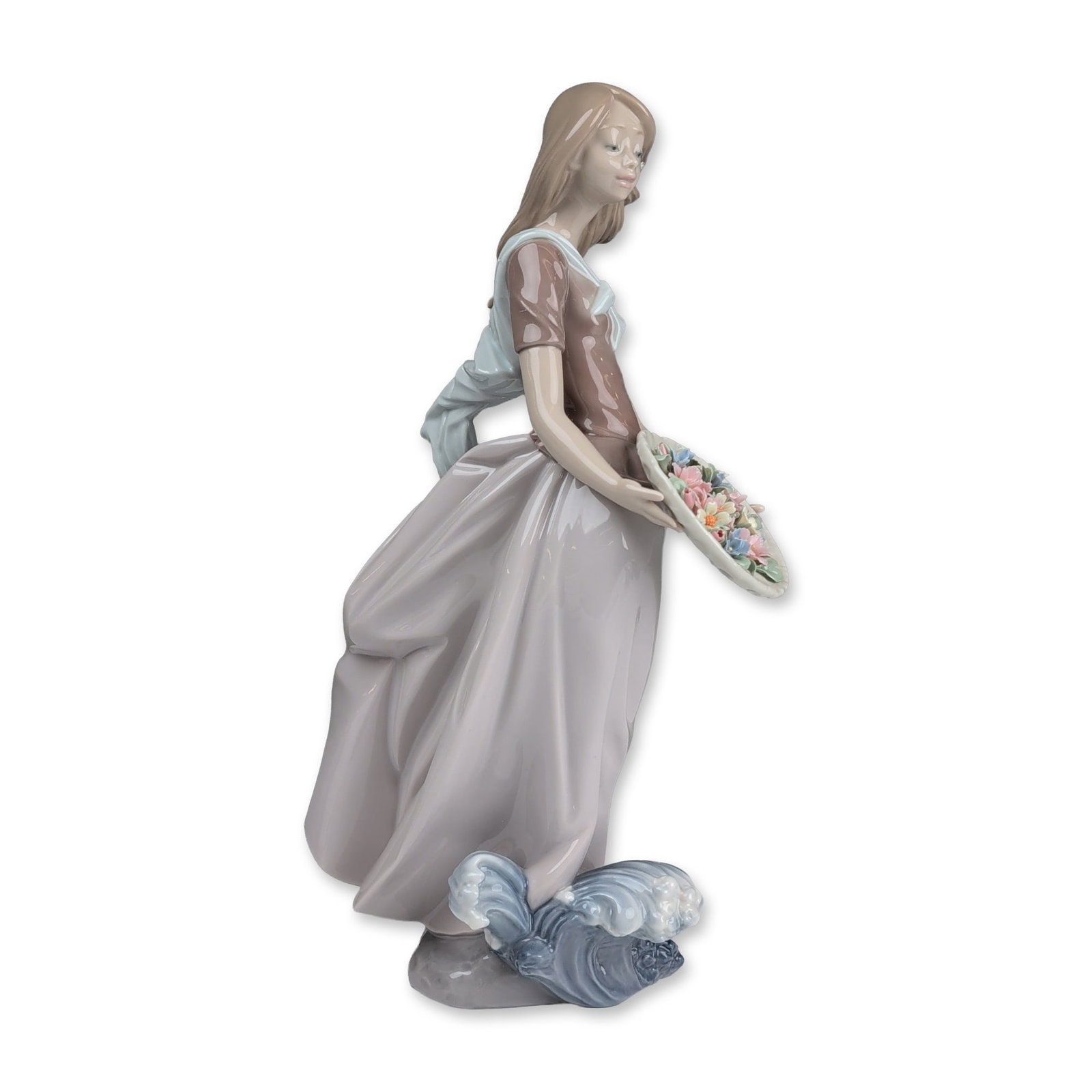 Lladro Porcelain Figurine, Ocean Offering 01006682: Glazed porcelain figurine designed by Salvador Debon. The piece depicts a young woman in a windswept pose, dressed in a brown bodice and lavender skirt with a light blue shawl draped over her