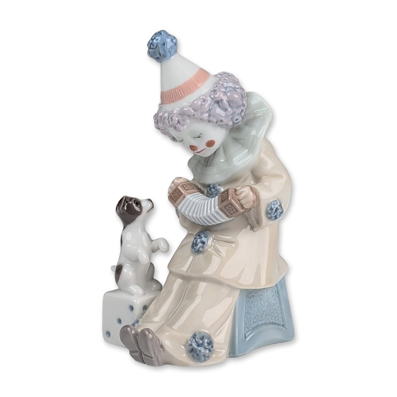 Lladro Porcelain Figurine, Pierrot with Concertina 01005279: Glazed porcelain figurine designed by Jose Puche depicts a seated Pierrot clown in a cream-colored suit accented with blue pom-poms, wearing a purple curly wig and a white pointed hat with pink bandin