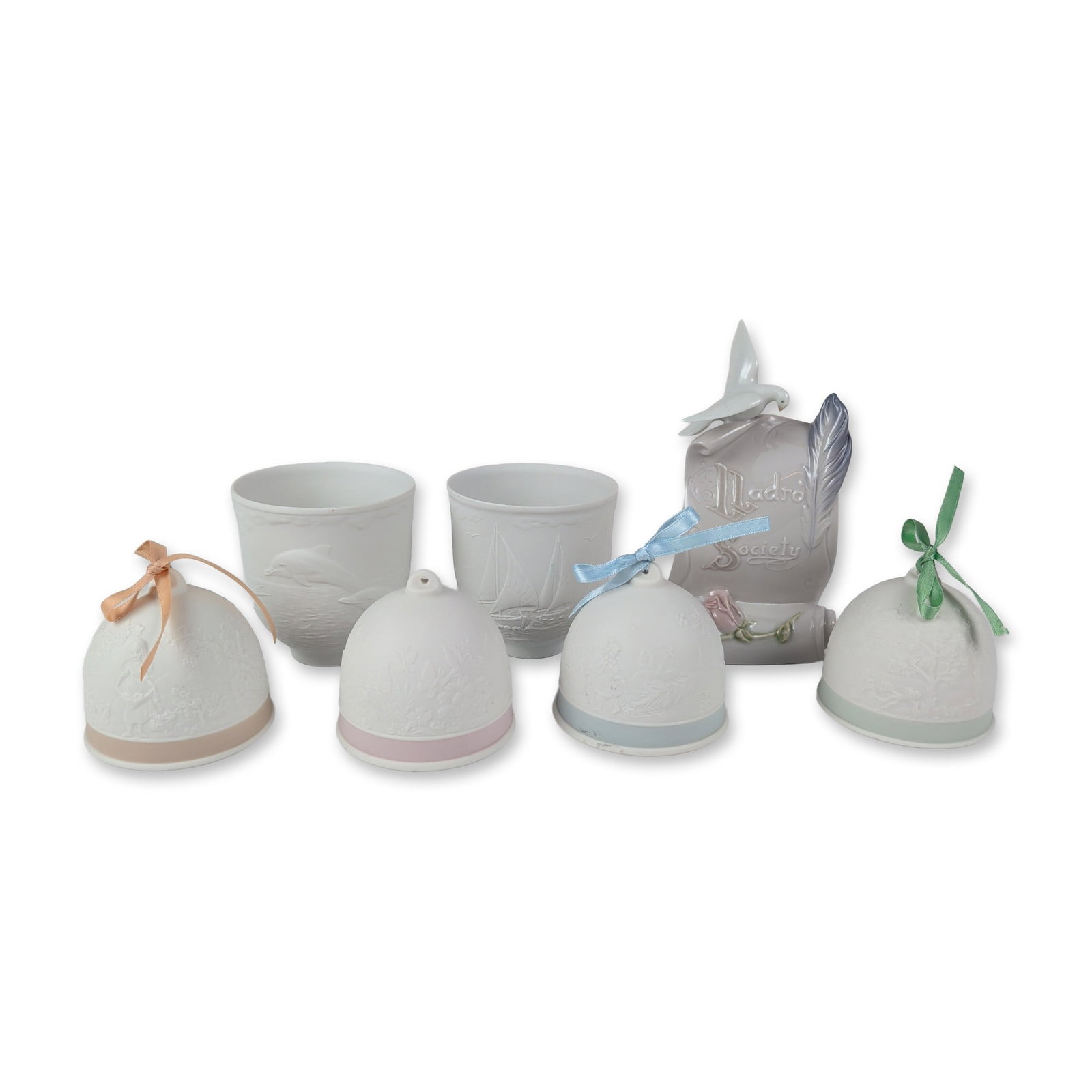 7pc Lladro Collectors Society Porcelain Items: Collection of seven Spanish porcelain decorative items produced for the Lladro Collectors Society, comprising one glazed plaque, four bisque bells, and two bisque votive cups. The scroll-form plaque f
