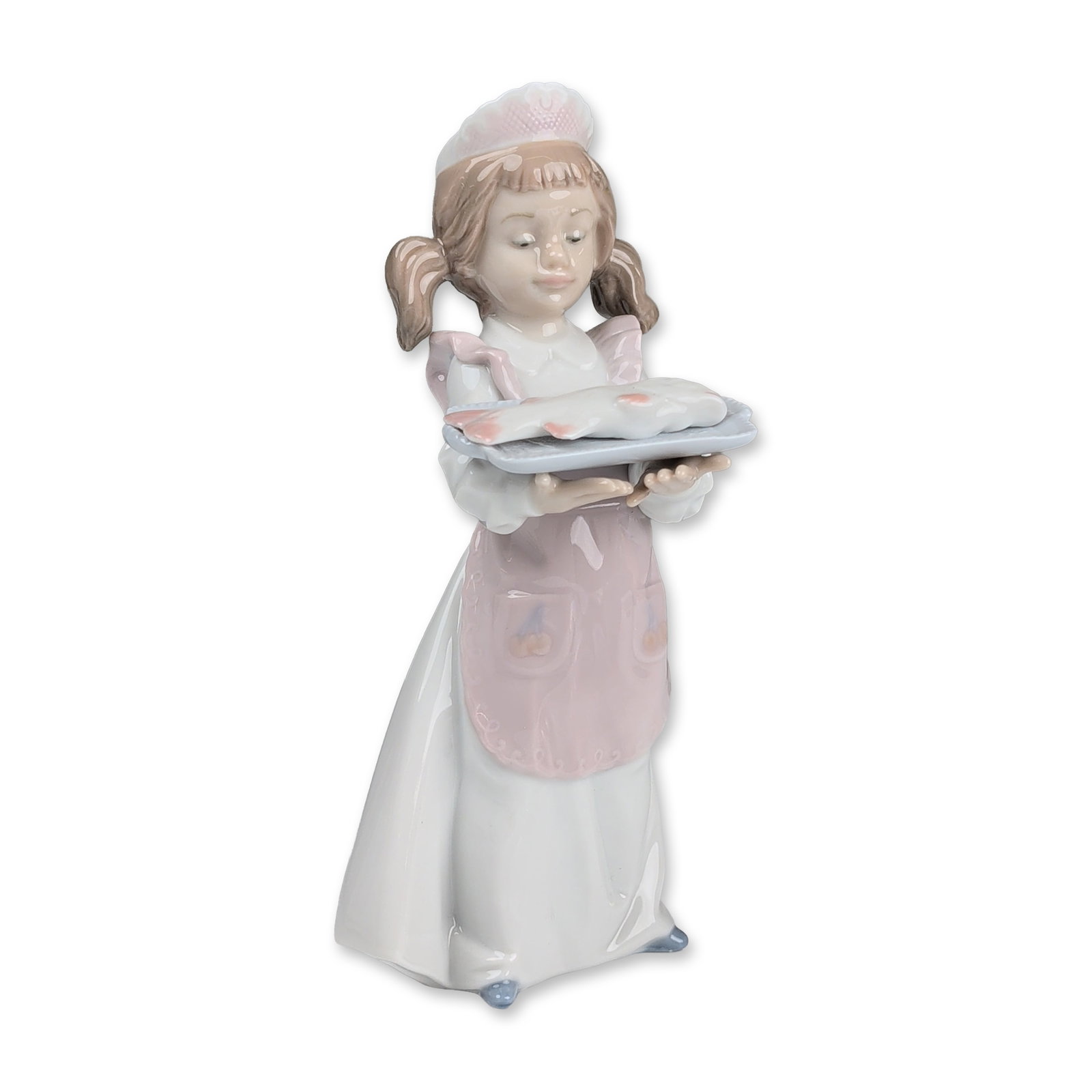 Lladro Glazed Porcelain Figurine, Dinner is Served 01006235: Glazed polychrome porcelain figurine designed by sculptor Antonio Ramos. The figure depicts a young girl with brown pigtails wearing a white dress, a pink ruffled apron with heart-shaped pockets, and 