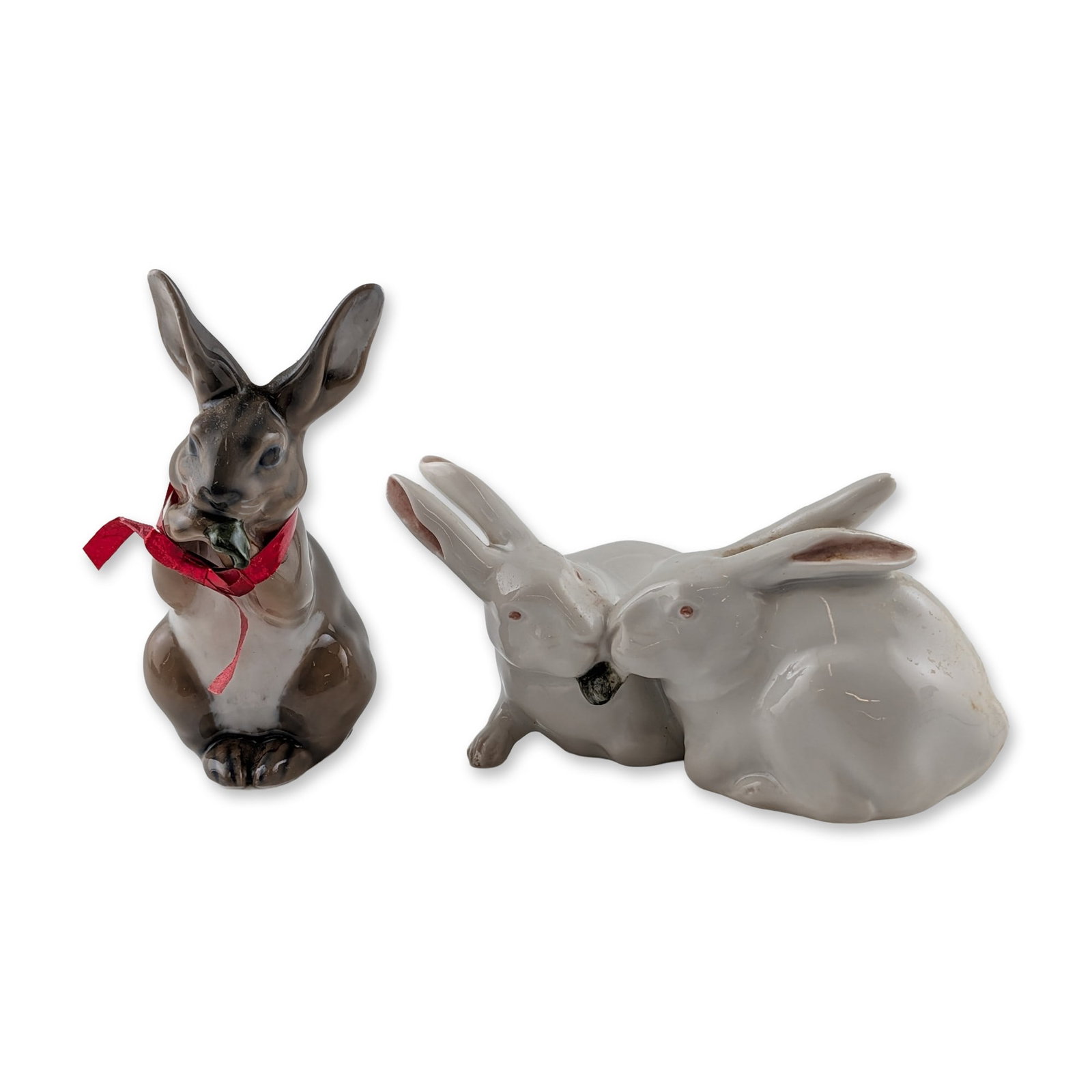 2pc Royal Copenhagen Danish Porcelain Rabbit Figurines: Royal Copenhagen, Denmark. Two glazed porcelain rabbit figurines. The first depicts a seated rabbit with a leaf in its mouth, model 1019, designed by Christian Thomsen. This figure features a brown an