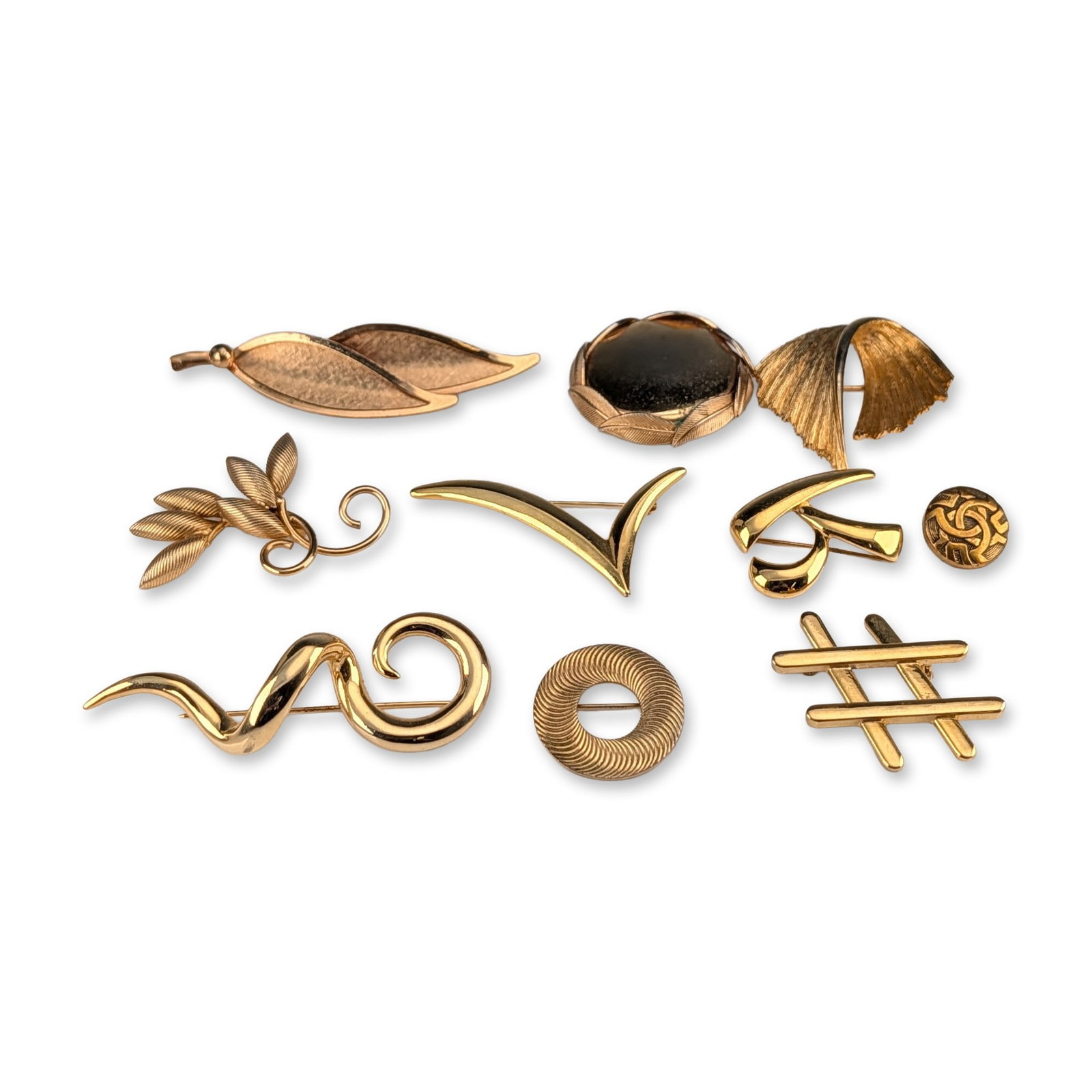 10pc Group of Vintage Gold Tone Brooches: Collection of ten vintage gold-tone costume jewelry brooches, featuring various botanical, modernist, and geometric motifs. The grouping includes a large double-leaf design, a leafy branch, a circular