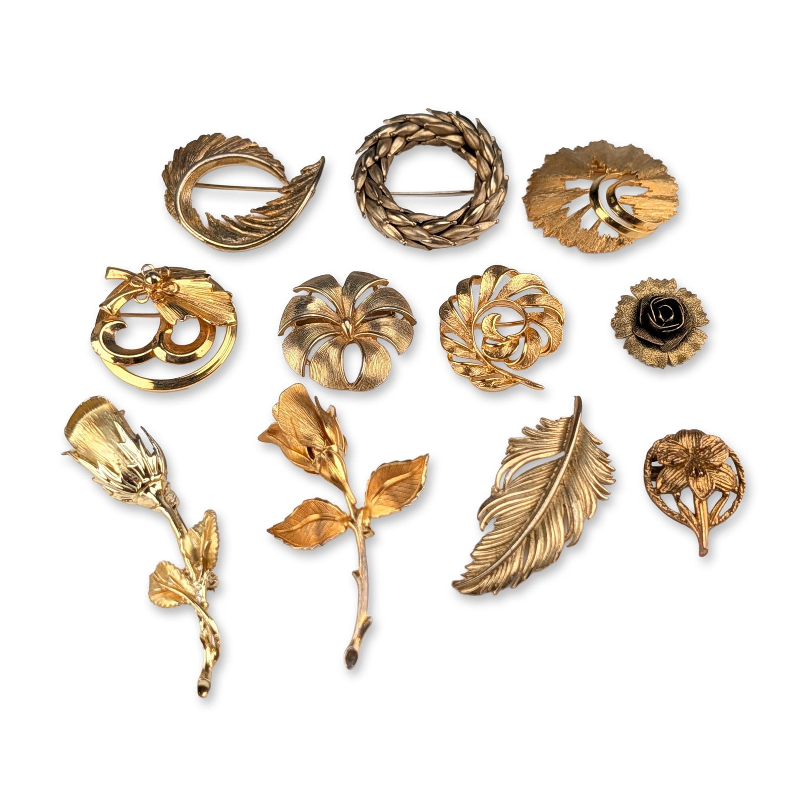 11pc Collection of Vintage Gold Tone Botanical Brooches: Collection of eleven vintage costume jewelry brooches in gold-tone base metal, featuring botanical and abstract motifs. The assortment includes wreath designs, multiple rose and rosebud forms, a curve