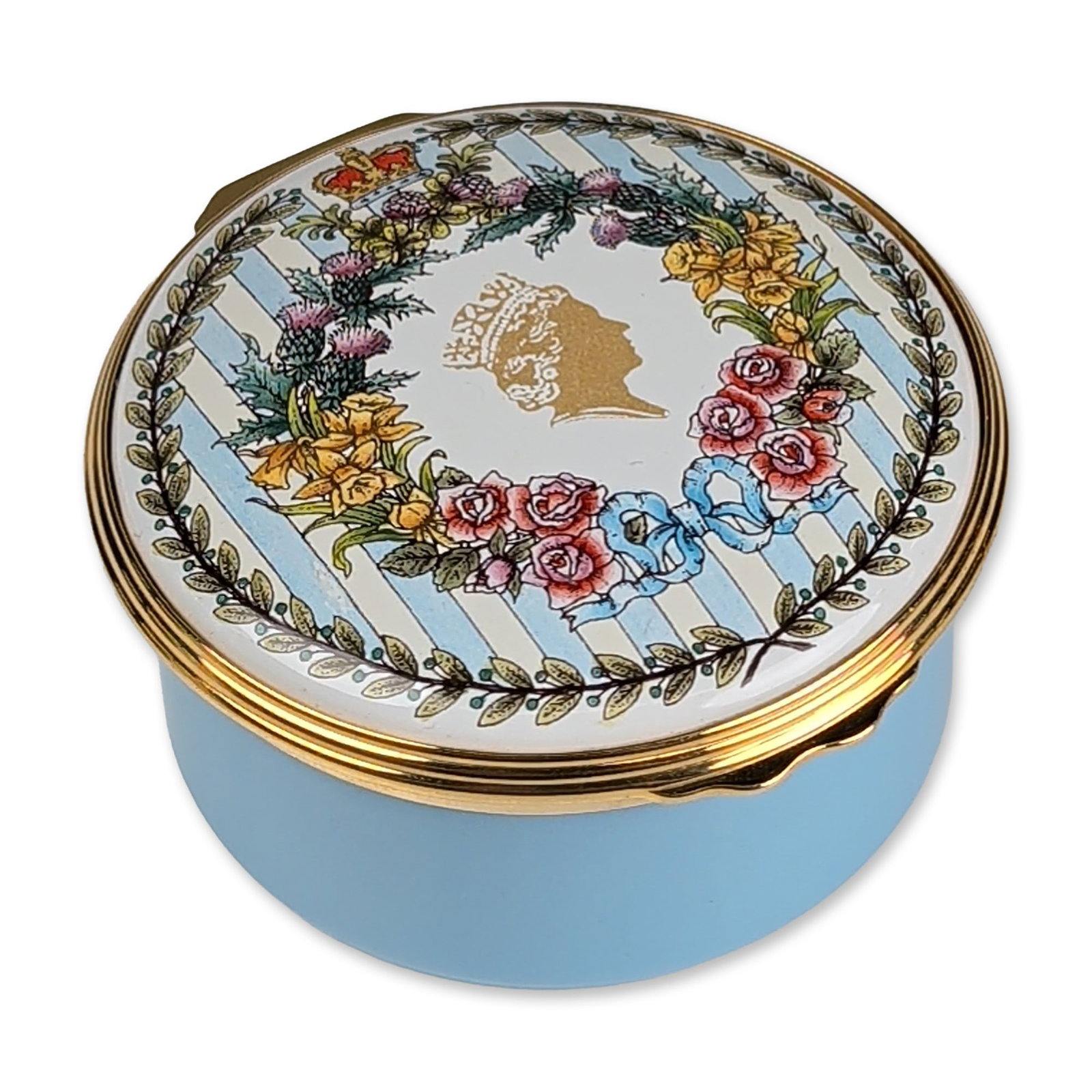 Halcyon Days God Save the Queen Diamond Jubilee Musical Enamel Box: Halcyon Days musical commemorative box in light blue enamel and gold-toned metal. Circular form with a hinged lid decorated with a floral wreath of roses, thistles, daffodils, and shamrocks surroundin