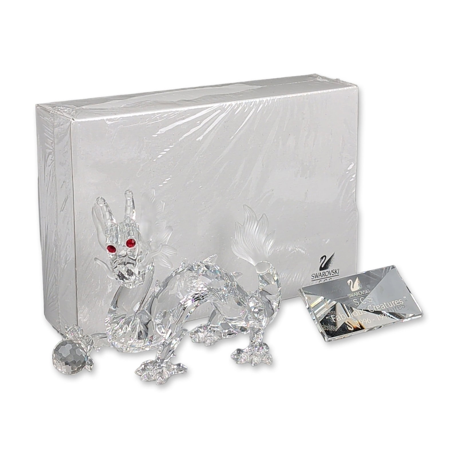 3pc Swarovski Crystal SCS 1997 Annual Edition Figurine, Dragon, Title Plaque & Base: The Dragon designed by Gabriele Stamey as part of the Fabulous Creatures trilogy. The clear faceted lead crystal figure is depicted in an undulating pose, clutching a faceted crystal ball and featurin
