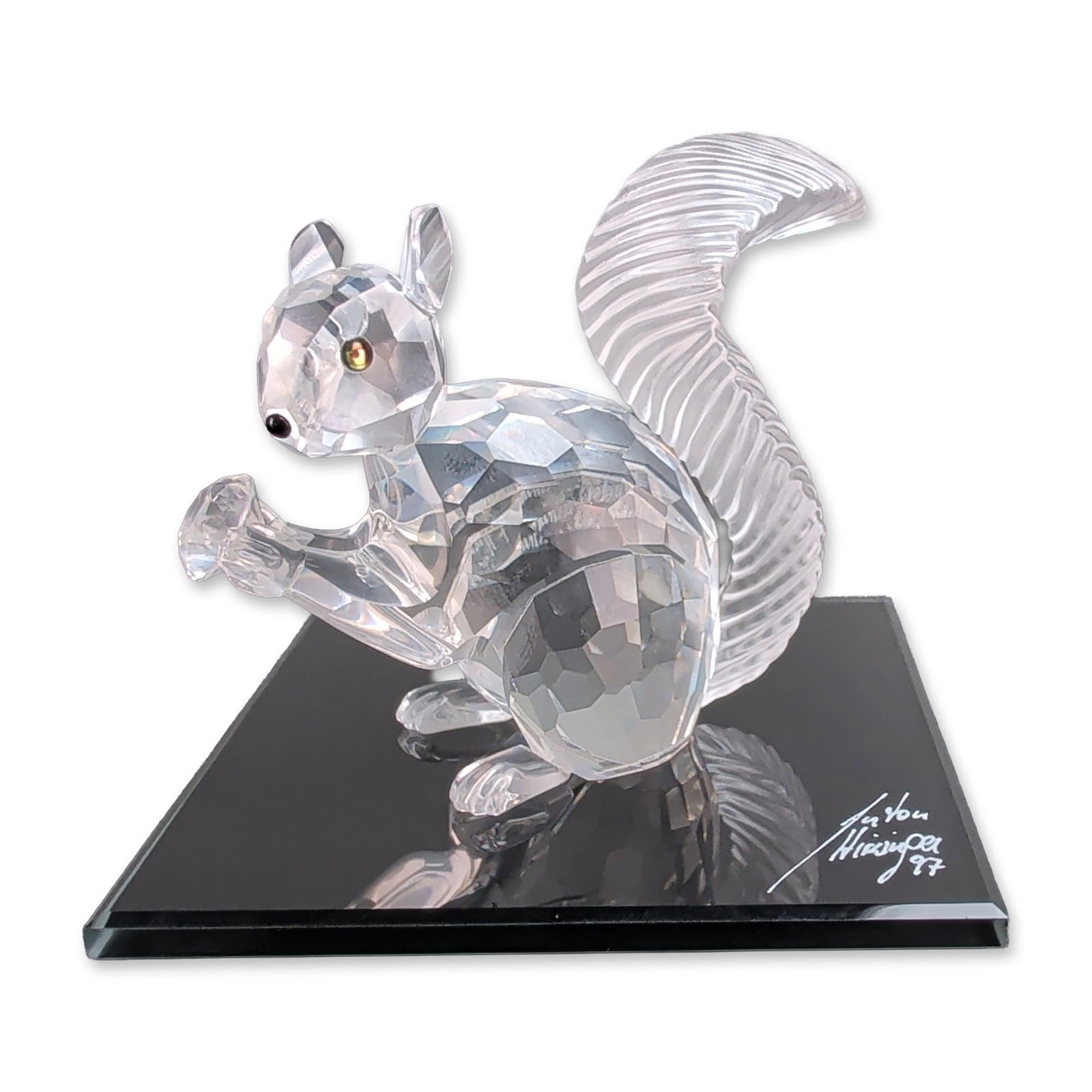 Swarovski 1997 SCS Crystal Squirrel Figurine with Mirror Base: Swarovski 1997 SCS Annual Edition featuring a squirrel figurine in faceted lead crystal with a frosted textured tail, dark inset crystal eyes, and depicted seating while holding an acorn. The undersid