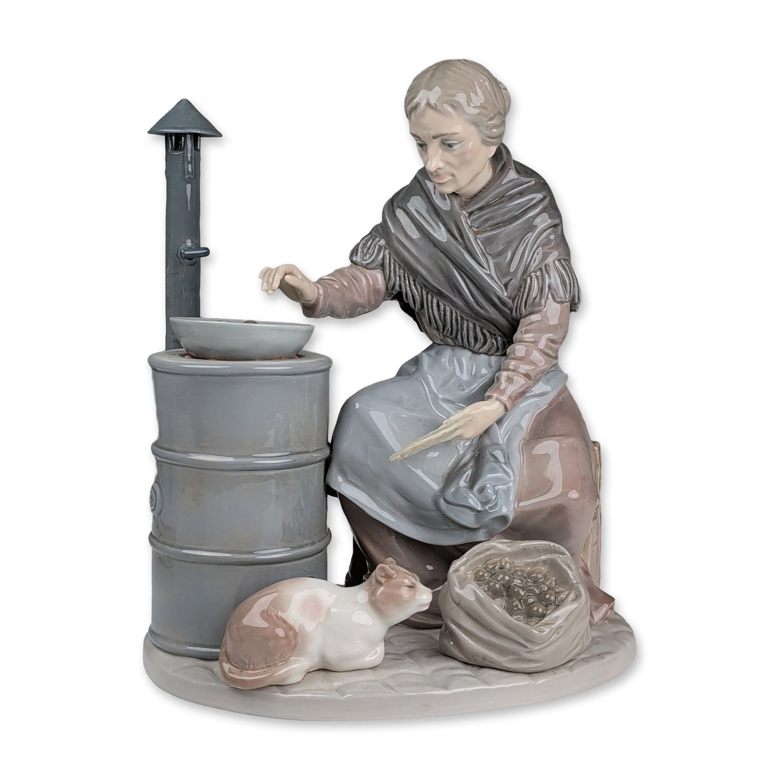 Lladro Glazed Porcelain Figurine, Chestnut Seller 01001373: Glazed porcelain figurine designed by Salvador Furio. The polychrome figure depicts an elderly woman wearing a gray fringed shawl over a brown and blue dress, crouching beside a cylindrical stove whil