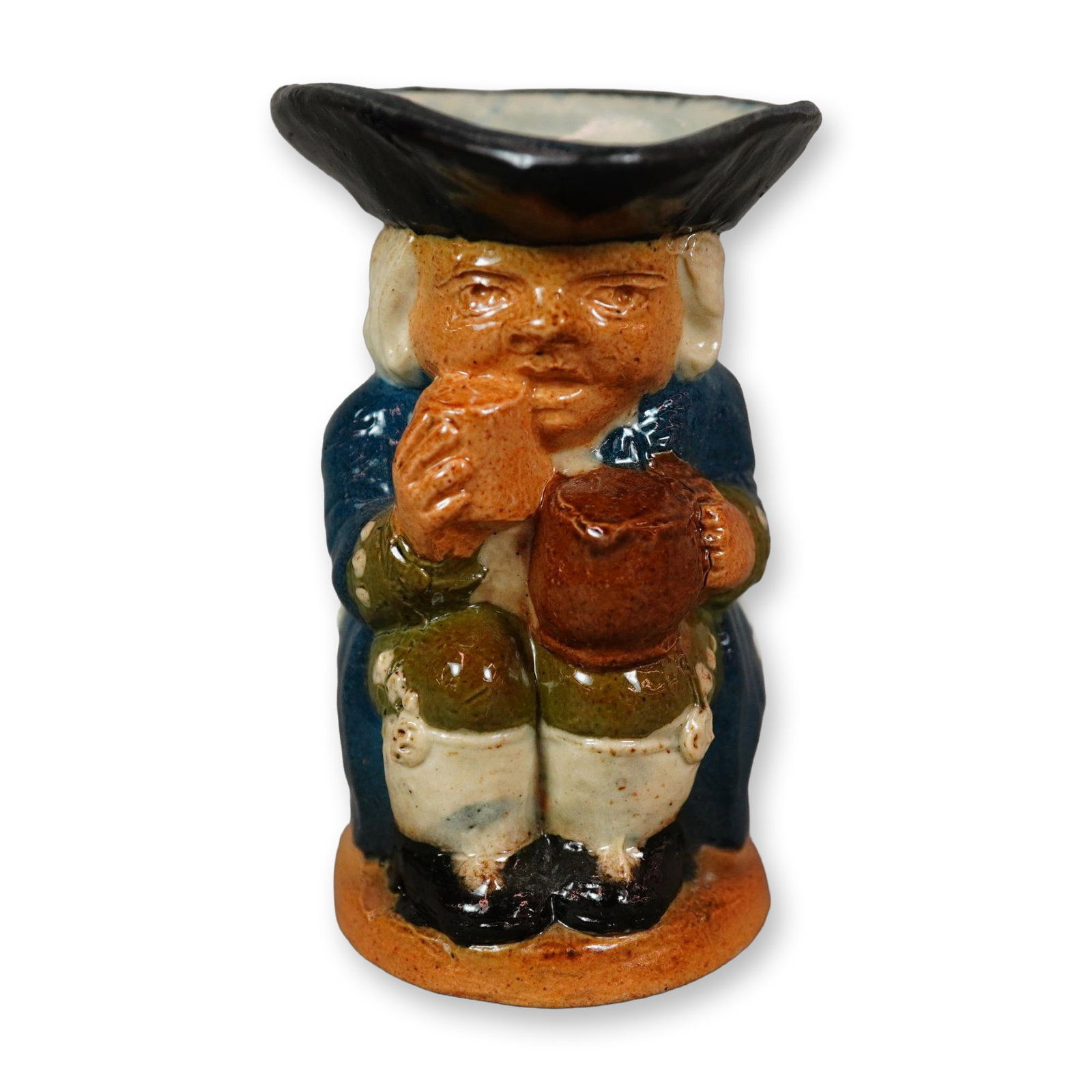Royal Doulton Lambeth Stoneware Salt-Glazed Ordinary Toby Jug: A figure jug depicting a seated man wearing a tricorn hat, resting a jug of ale on his knee. He is dressed in a blue coat with green cuffs and trousers, and a black hat. The handle is a plain brown fi