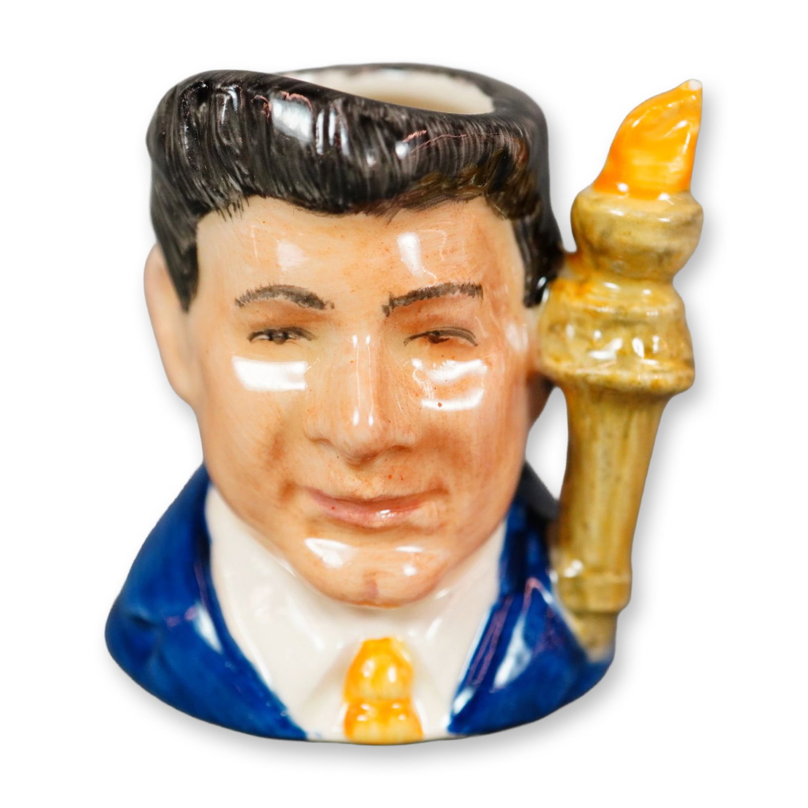 Royal Doulton Prototype Colorway Tiny Character Jug, John F. Kennedy: Figural jug depicting John F. Kennedy, shown wearing a blue coat with a yellow tie and dark-gray hair. Handle modeled as a flaming torch. Features Royal Doulton backstamp. Dimensions: 1.5"L x 1.25"W x