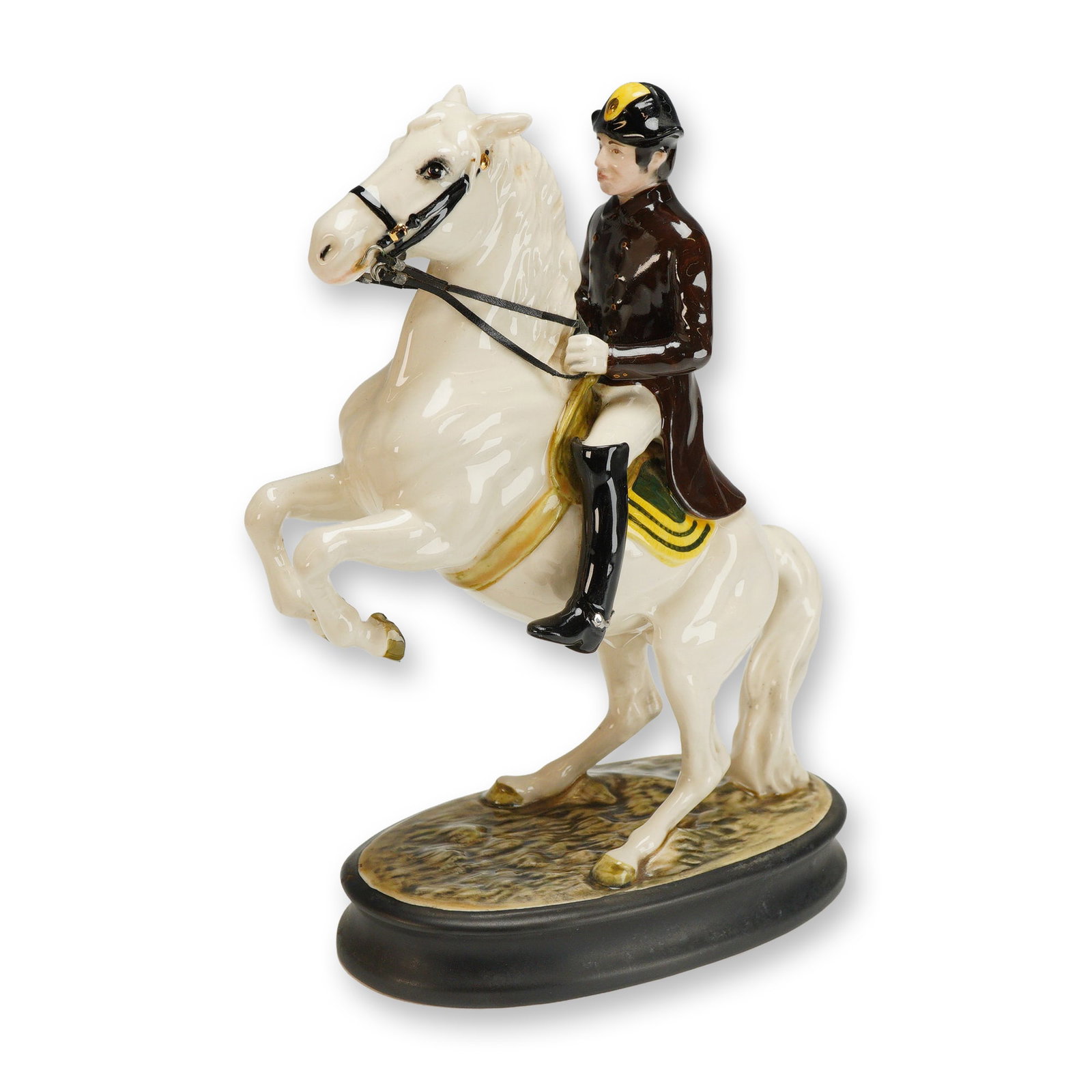 Beswick Porcelain Figurine, Lipizzaner with Rider: A glazed porcelain figure depicting a rider on a rearing horse, mounted on an oval base. The rider wears a brown top, beige pants, and black boots. The horse has a white coat and wears a yellow and gr