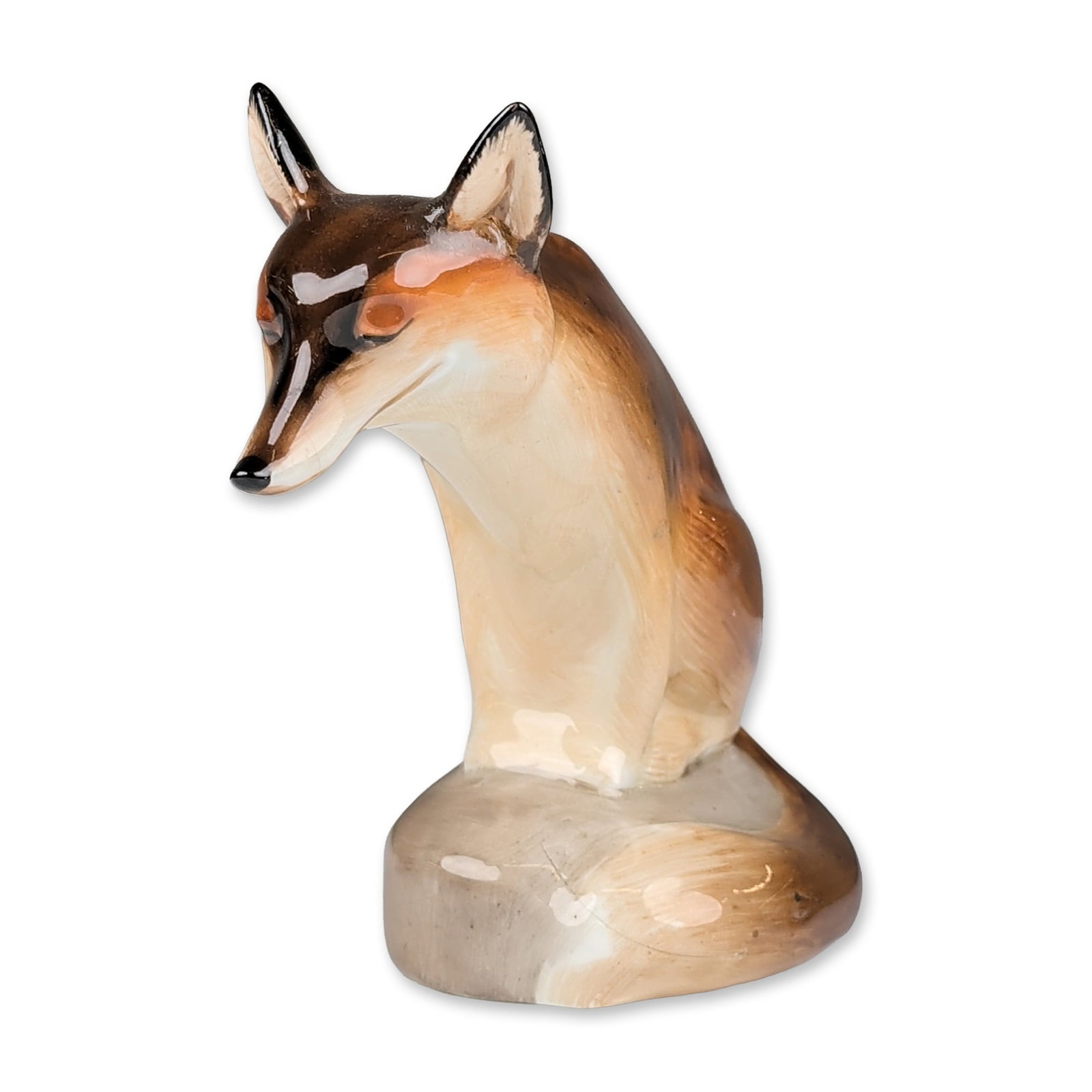 Royal Doulton Porcelain Figurine, Fox Seated: Fox figurine in a high-gloss glaze, featuring a naturalistic palette of russet brown and cream tones with black hand-painted details to the ears, nose, and eyes. The figure is modeled in a seated pose