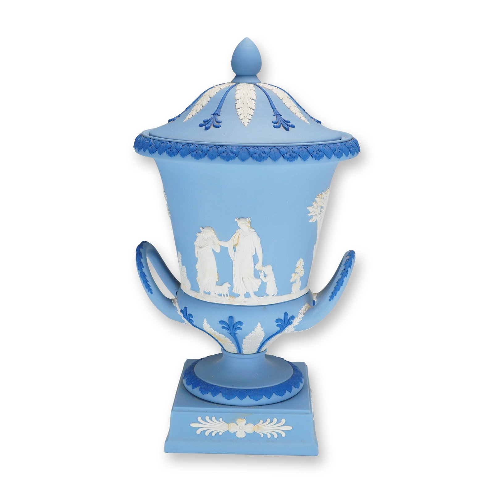 Wedgwood Light Blue Jasperware Campagna Pedestal Urn and Cover: A Wedgwood tri-color Jasperware lidded urn of campagna form featuring a light blue dip ground. The body is decorated with applied white bas-relief sprigged scenes depicting classical figures and trees