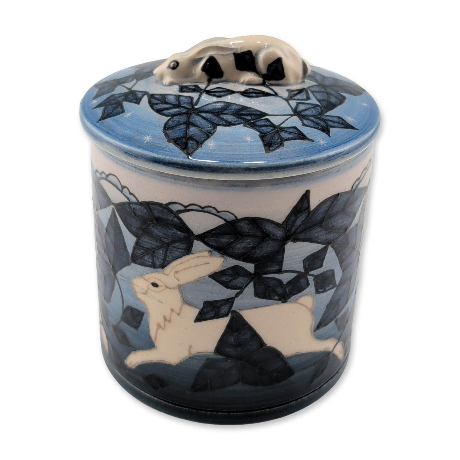 Dennis Chinaworks by Sally Tuffin Lidded Jar, Moonlit Hare: Lidded cylindrical jar in earthenware, featuring an Arts and Crafts style design by Sally Tuffin. The exterior is decorated with running hares within stylized cobalt and navy blue foliage on a cream g