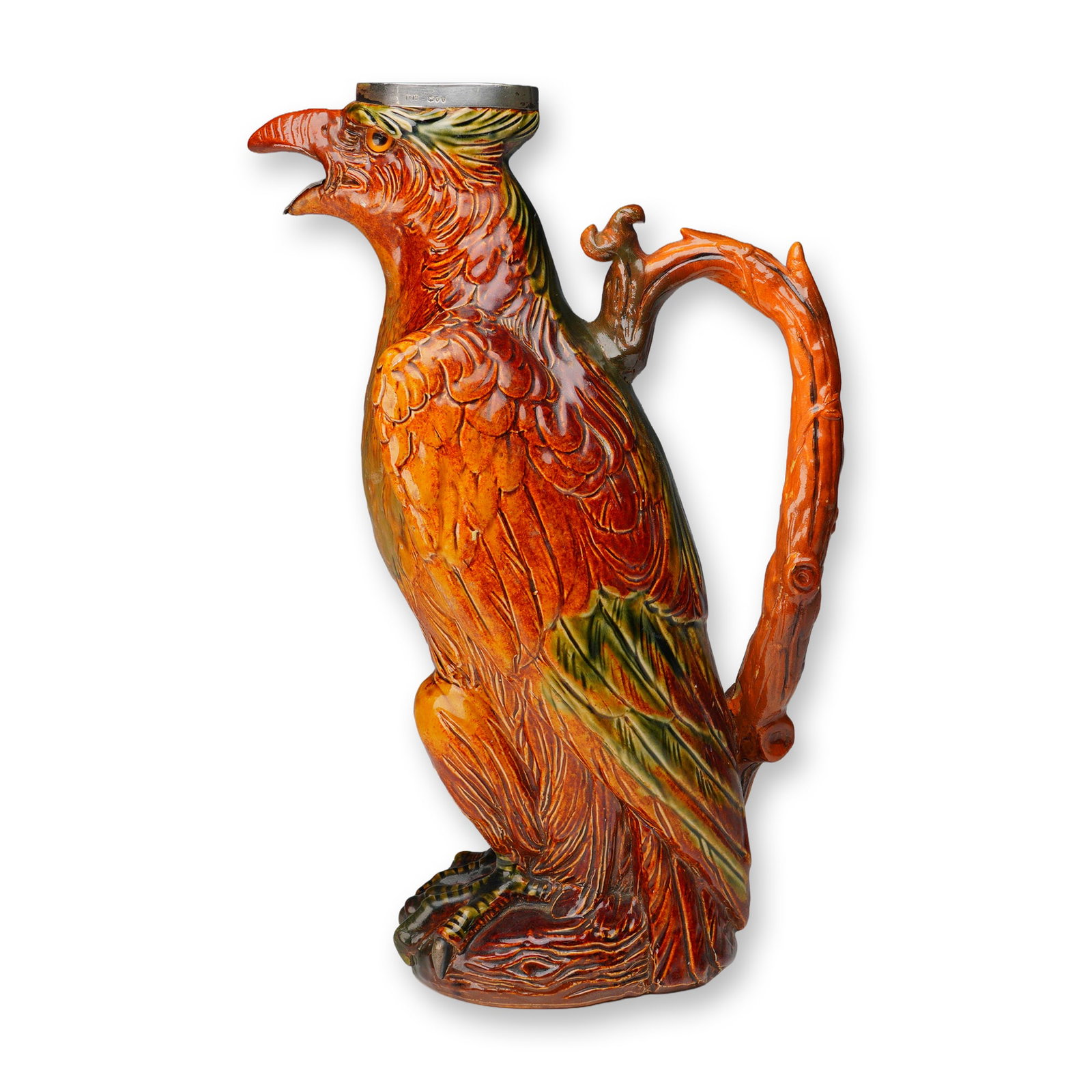 Doulton Lambeth Stoneware and Sterling Silver Decorative Eagle Jug: Figural jug modeled in the form of a perched eagle with finely detailed plumage, talons, and beak, rendered in richly colored stoneware with deep russet, green, and ochre glaze. The eagle's beak and r