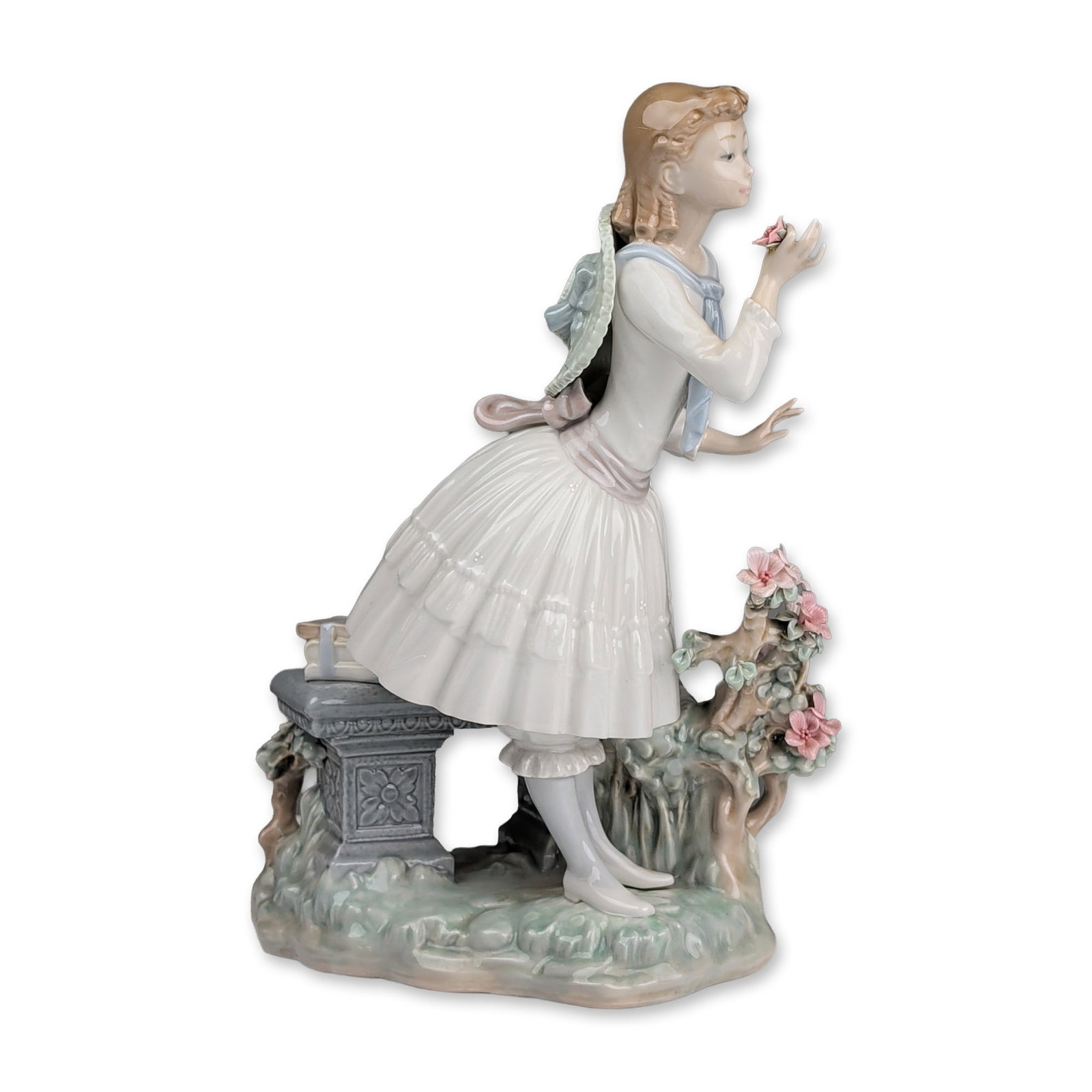 Lladro Porcelain Figurine, Exquisite Scent 01001313: The polychrome glazed piece, designed by Vincente Martinez. depicts a young woman in late 19th-century attire, featuring a voluminous white tiered skirt, lavender-pink waist sash, and light blue necke