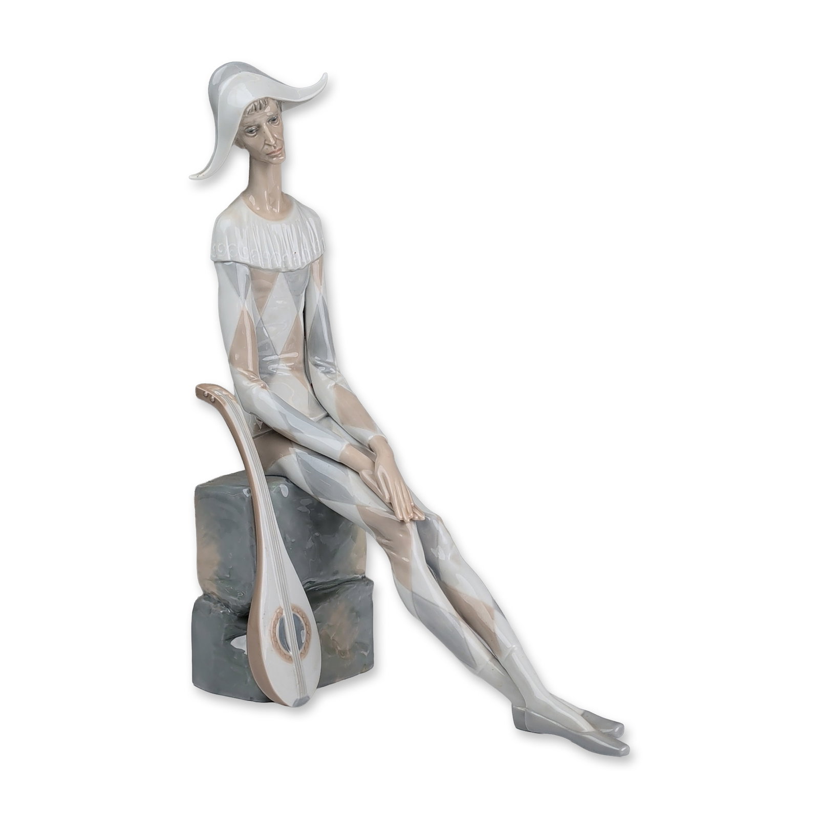 Lladro Porcelain Figurine, Sad Harlequin 01004558: Large porcelain figurine designed by Fulgencio Garcia. The polychrome glazed figure is depicted in an elongated seated pose against stacked blocks, wearing a traditional harlequin costume with a pale 