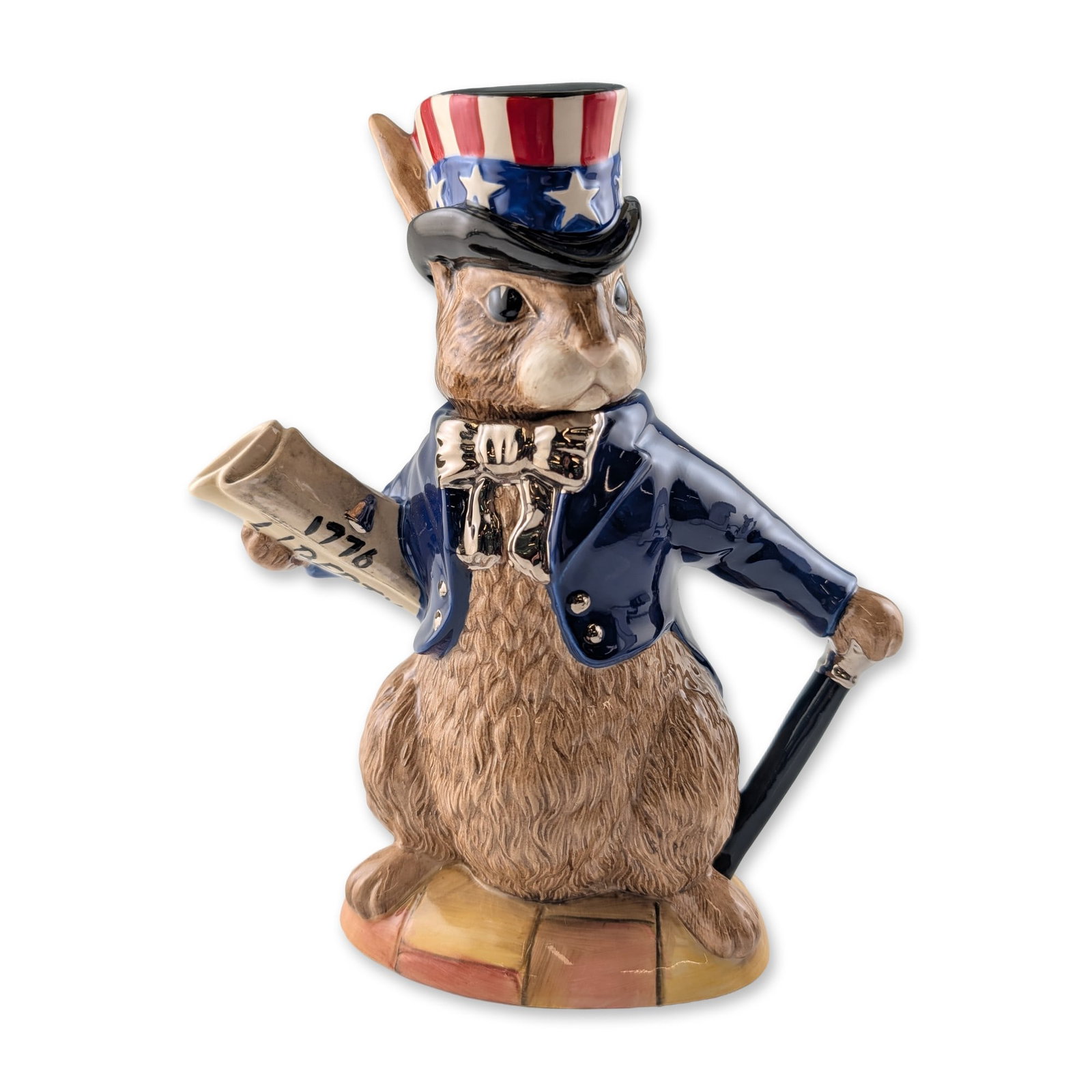 Royal Doulton Bunnykins Prototype Teapot, USA President D6996: The glazed ceramic vessel is modeled as an anthropomorphic rabbit dressed in the likeness of Uncle Sam, wearing a navy-blue tailcoat with silver-tone buttons and a stars and stripes top hat. A rolled 