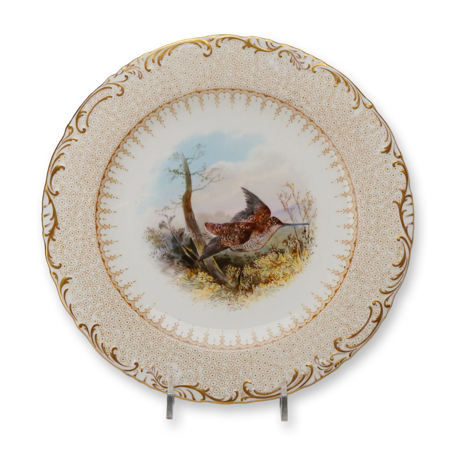 Wedgwood Hand-Painted Bone China Woodcock Cabinet Plate, circa 1900: A bone china cabinet plate featuring a central hand-painted medallion of a woodcock bird in flight over a marsh landscape. The naturalistic scene is rendered in soft brown, beige, and blue tones. The 