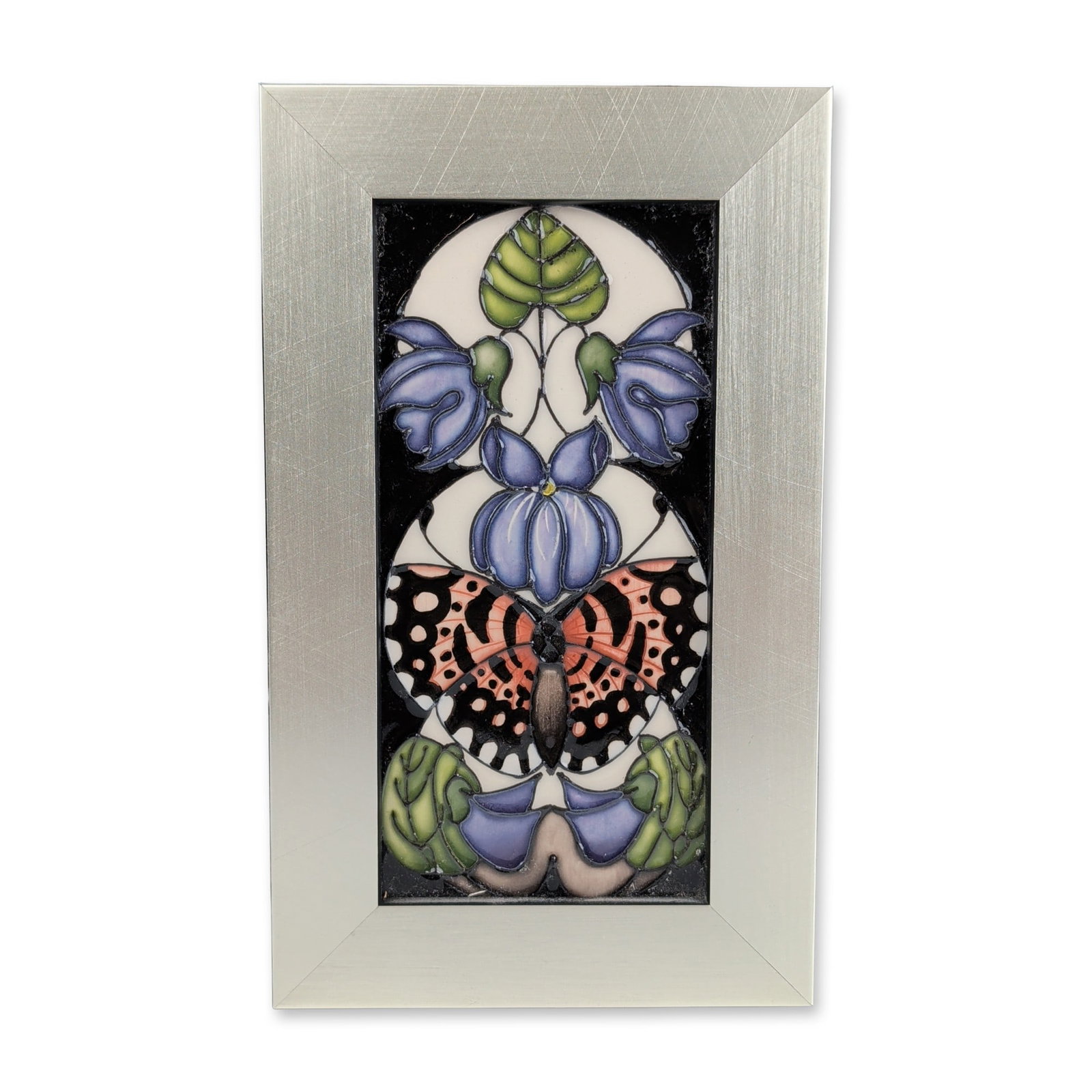 Moorcroft Pottery by Vicky Lovatt Framed Bluebell and Butterfly Tile: A tube-lined design featuring a central orange and black butterfly with bluebell flowers and green foliage. The composition is set within two overlapping circular frames against a solid black ground. 