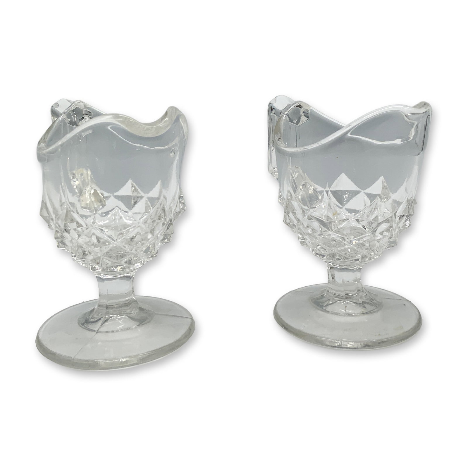 Pair of Art Glass Children's Creamer Jugs: Adorable duo of sawtooth variation clear glass jugs with handles and footing. Dimensions: 3.25"L x 2"W x 3"H Date or Era: 20th century
