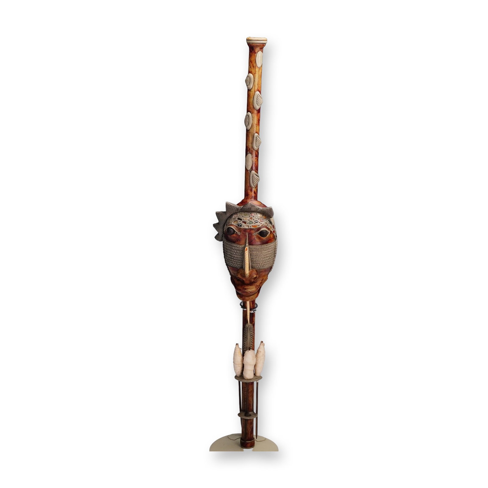 African Style Carved Wooden Staff Sculpture: Striking carved wooden staff sculpture featuring an elaborate mask face with intricate patterns and raised elements, accented by inset shells and beads, creating expressive eyes and a prominent centra
