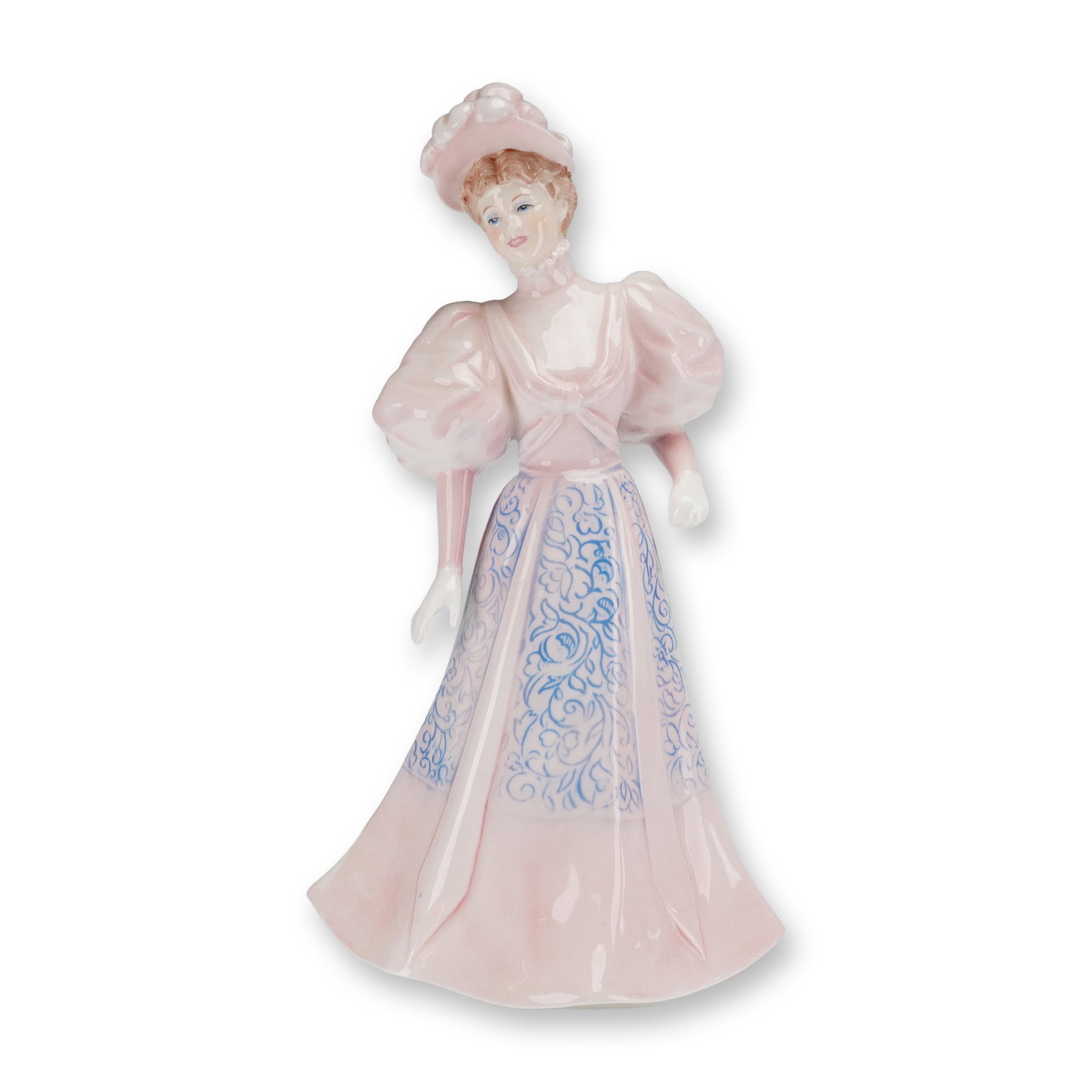 Coalport Bone China Figurine, Eugenie: The figure is modeled in a late Victorian style gown with a pale pink glaze. The dress features large, puffed sleeves and an inset skirt panel decorated with a blue floral scroll pattern. A blue sash 