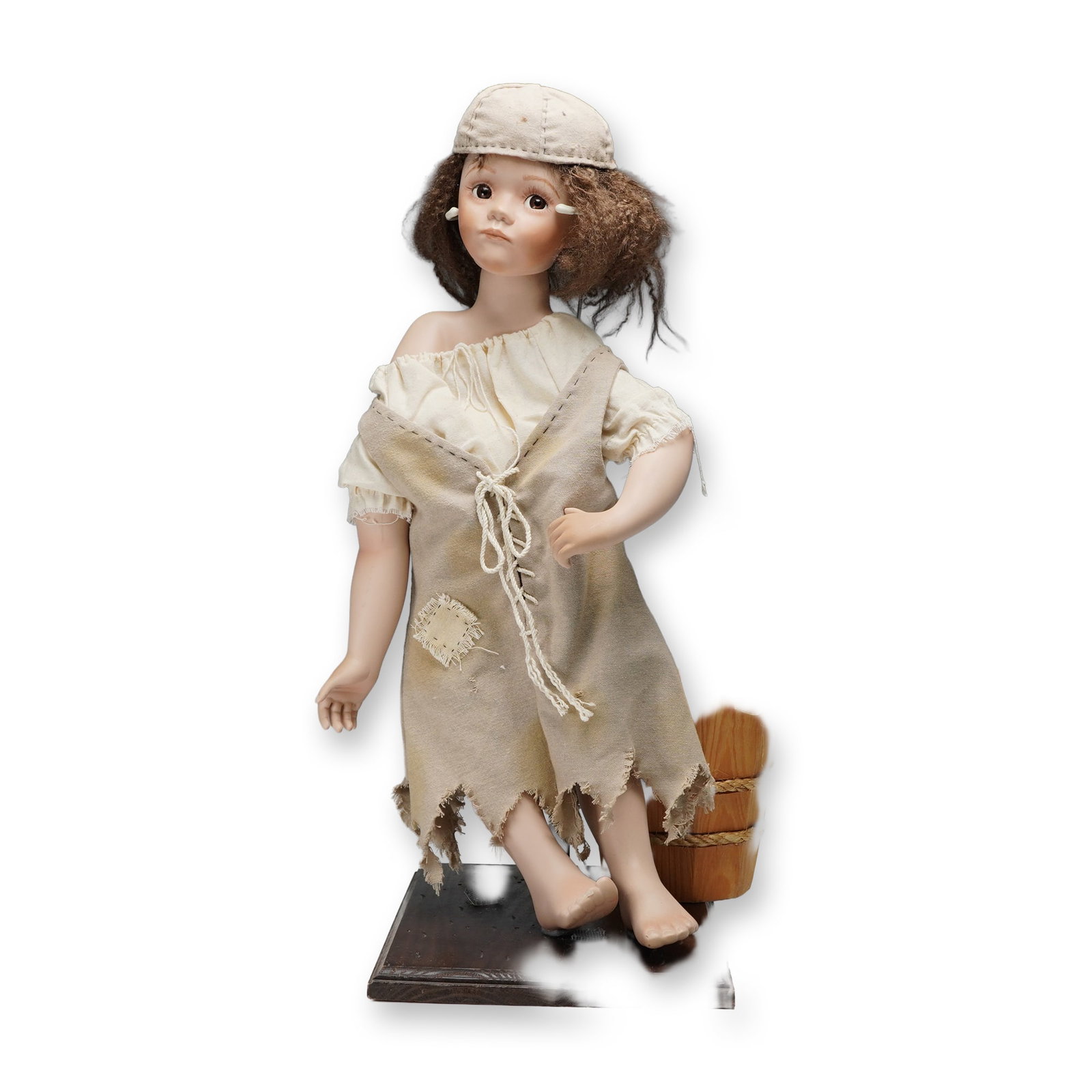 2pc Helen M. Carr Hamilton Collection Doll & Bucket, Ashley McTiddle: A finely crafted porcelain doll depicting a young girl in tattered period attire, posed & affixed on a wooden base with a rustic bucket accessory. The figure features expressive brown eyes, hand-paint