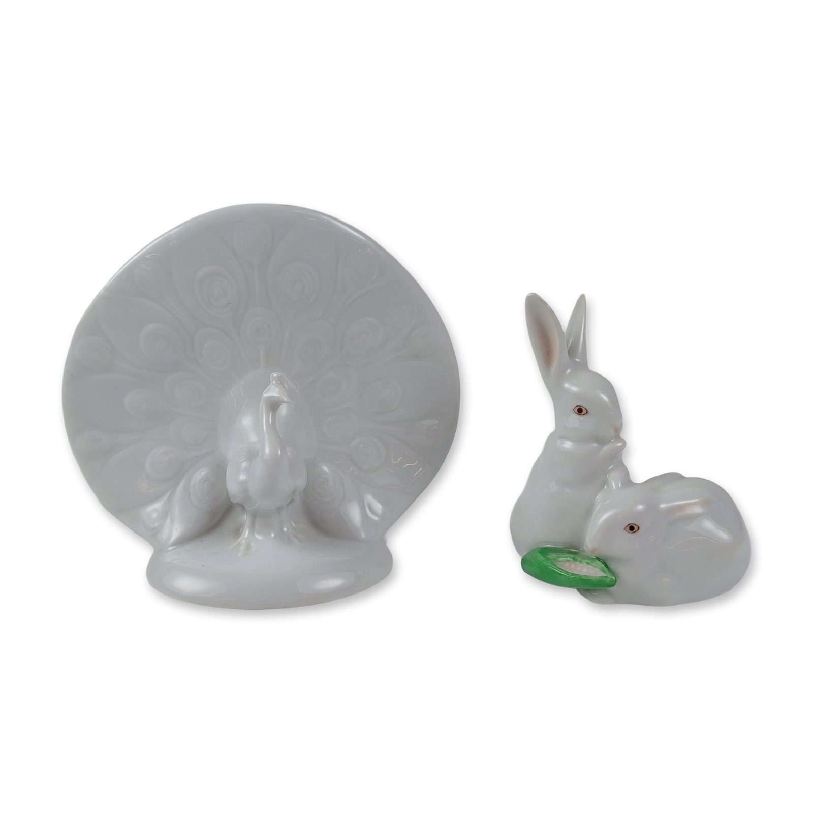 2pc of Herend Hungary Porcelain Peacock and Rabbits Figurines: Herend, Hungary. Two animal figurines in glazed white porcelain. One figurine depicts a pair of huddled rabbits with hand-painted reddish-pink eyes, one shown nibbling a green leaf. The second