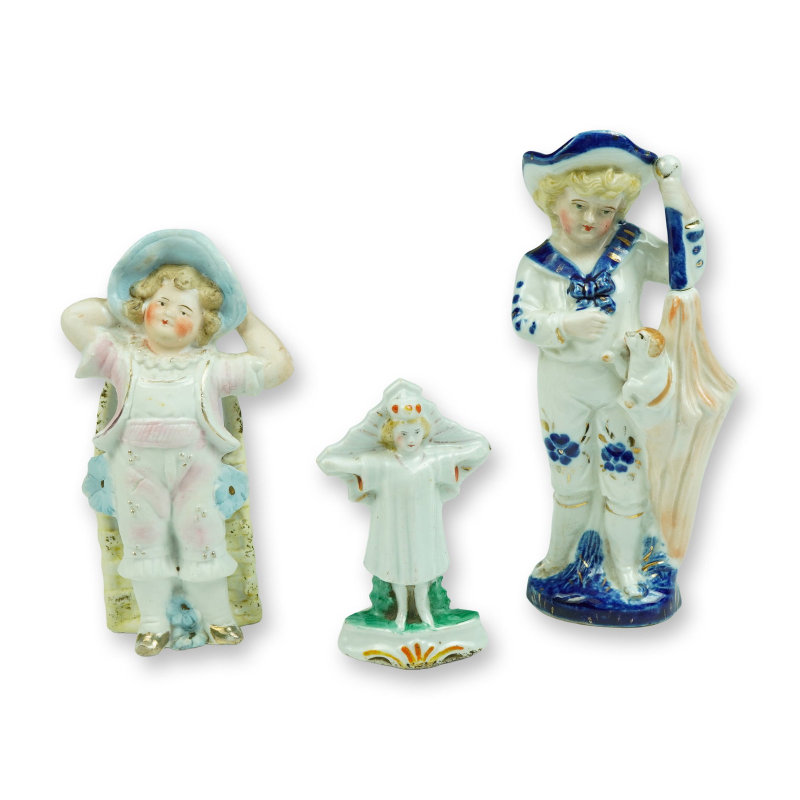 Porcelain Children Figurines: An utterly charming trio of figural fairings depicting children in whimsical poses, each crafted with delightful detail and hand-painted charm. The group includes a young boy in a pastel pink suit wit