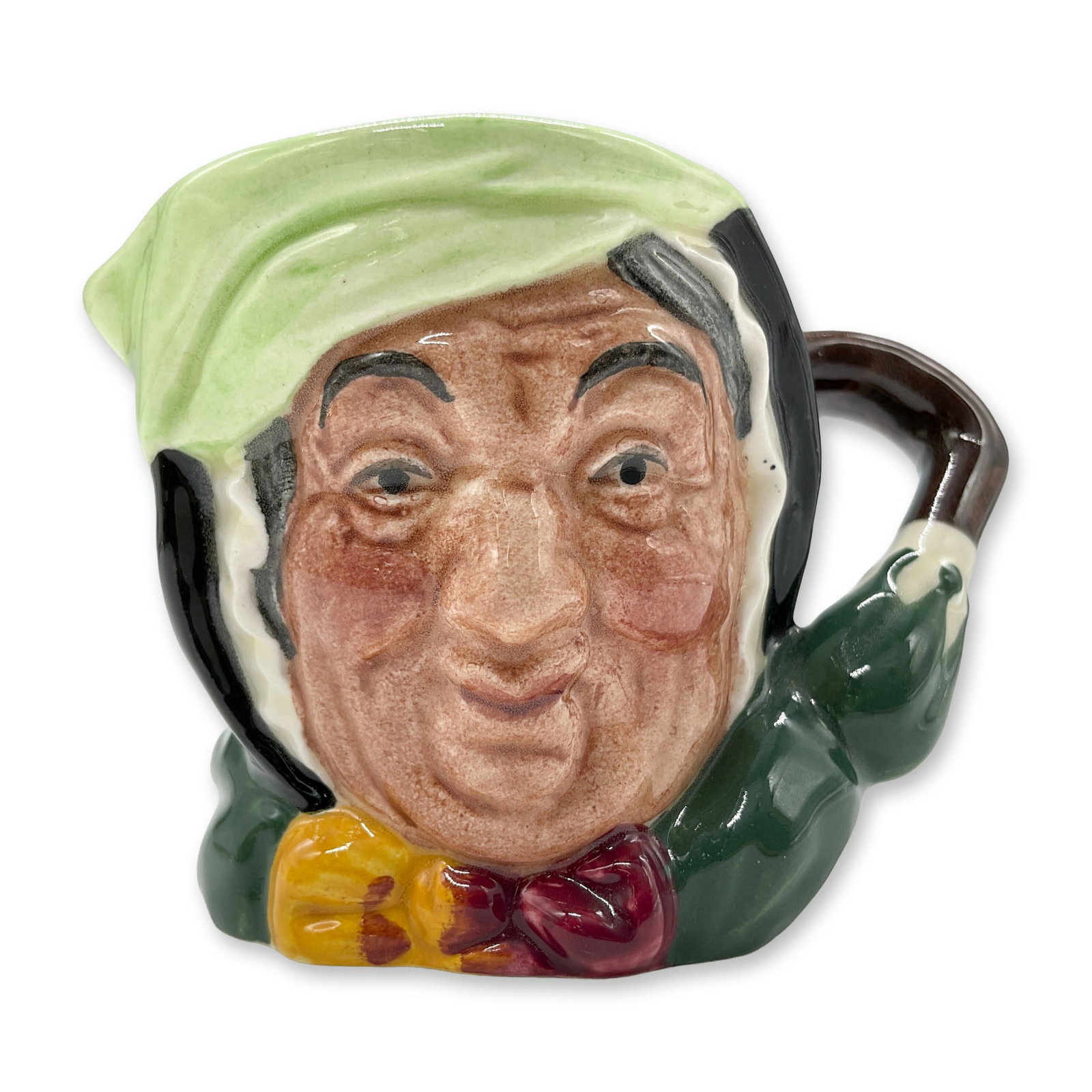 Sairey Gamp D6045 - Mini - Royal Doulton Character Jug: Black hair; light green band; dark green coat; yellow and burgundy bow. Royal Doulton backstamp. Artist: Leslie Harradine and Harry Fenton Dimensions: 3"L x 2"W x 2.25"H Date or Era: 1939 - 1986 Manuf