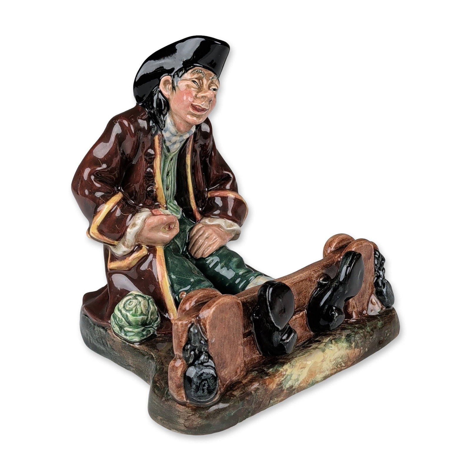 Royal Doulton Colorway Porcelain Figurine, In The Stocks HN2163: Designed by Mary Nicoll. The figure depicts a seated man in 18th-century attire including a black tricorn hat and long brown frock coat, his legs secured within wooden stocks with cabbages at the base